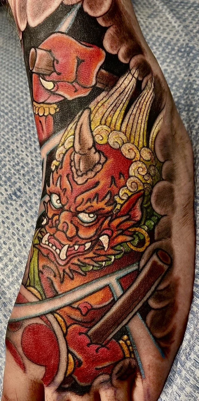 Colorful tattoo on arm featuring a fierce demon with sharp teeth, a unicorn horn, and a mixture of swirling patterns and flames.