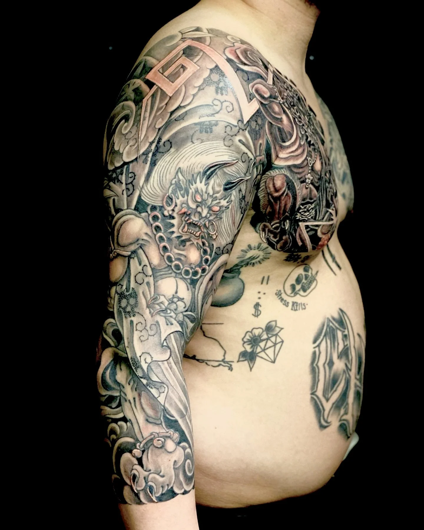 Tattooed upper body with a prominent Japanese-style lion, clouds, and various symbols and text on the chest and arm.