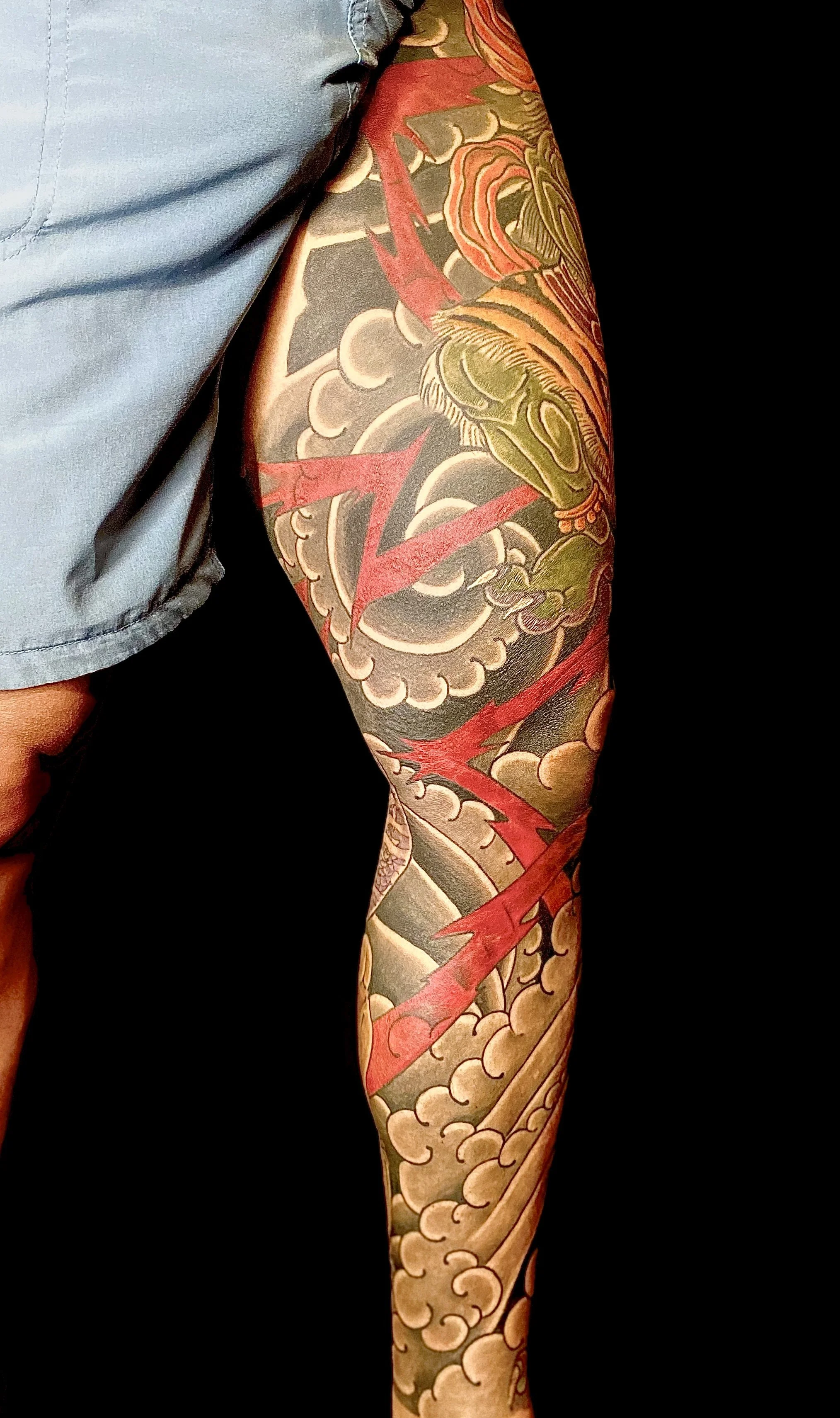 Colorful sleeve tattoo featuring a snarling dragon among clouds and lightning bolts on a person's arm.