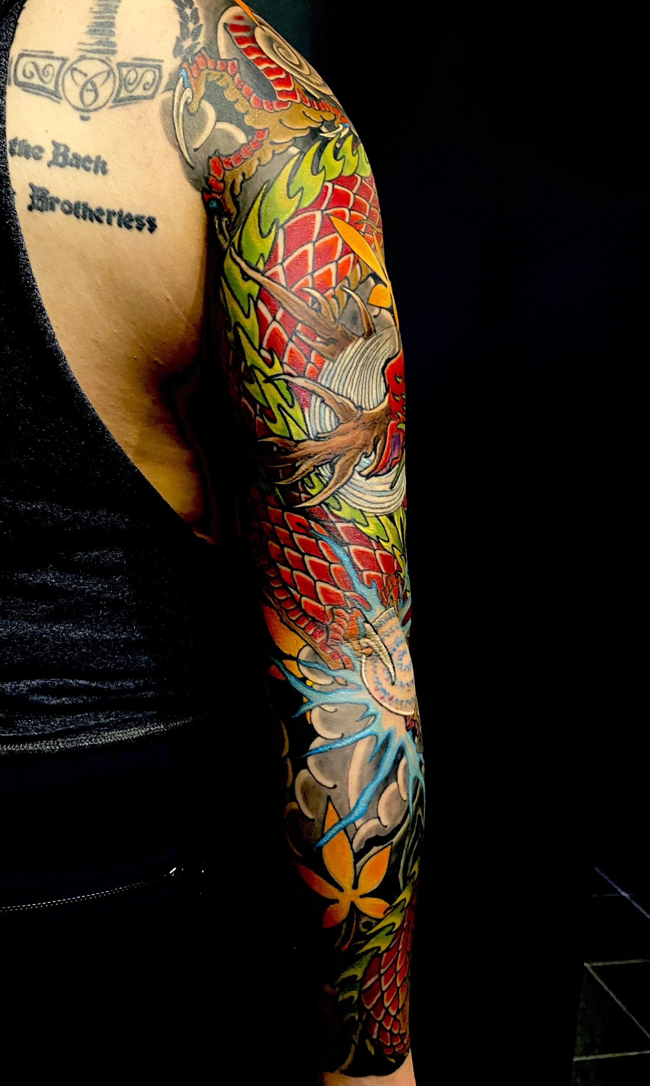 Close-up of a person's arm covered in colorful traditional Japanese-style tattoo featuring a dragon and floral elements.
