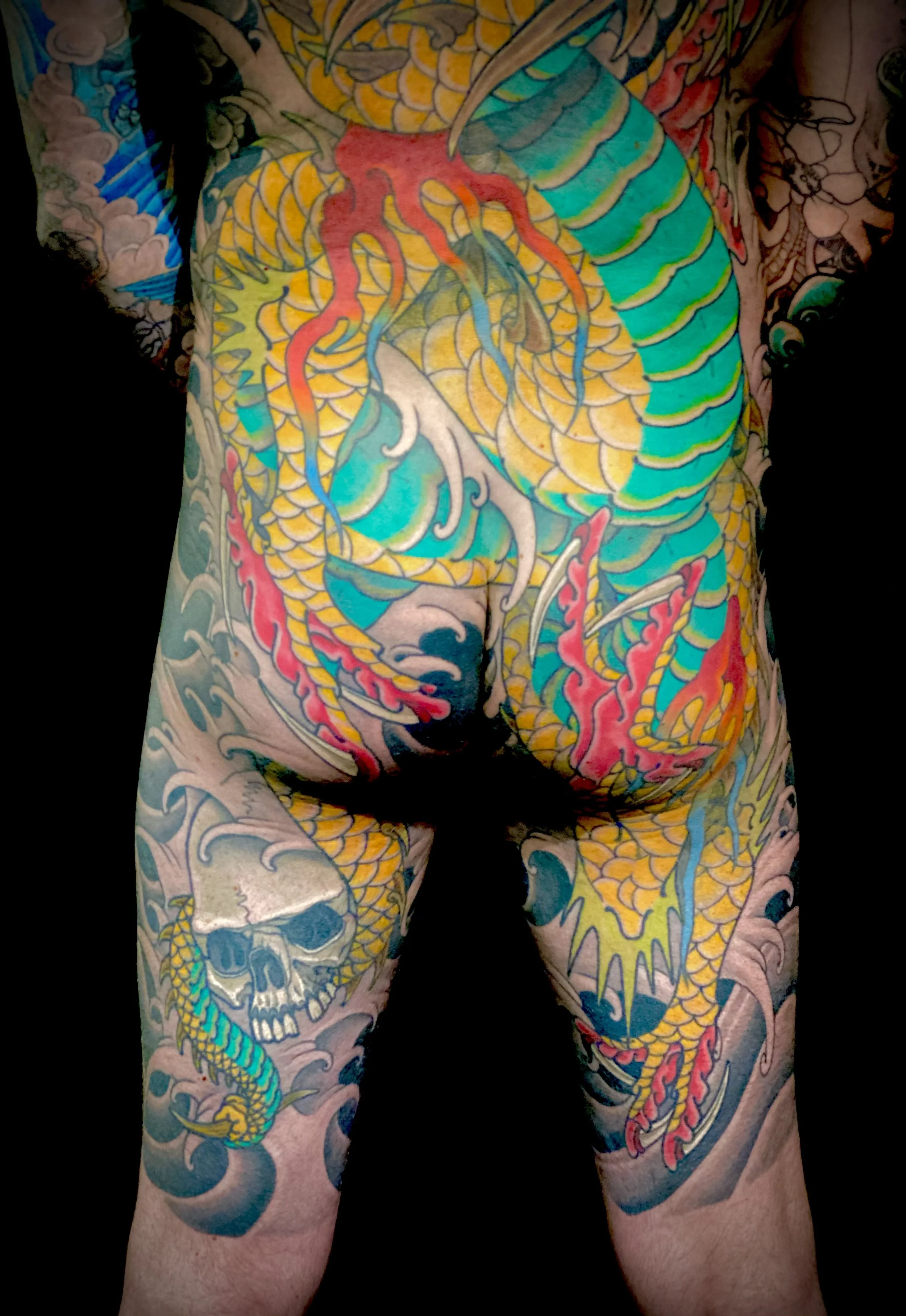 Colorful tattoo covering the person's back, torso, and thighs, featuring a dragon, a skull, and flames.
