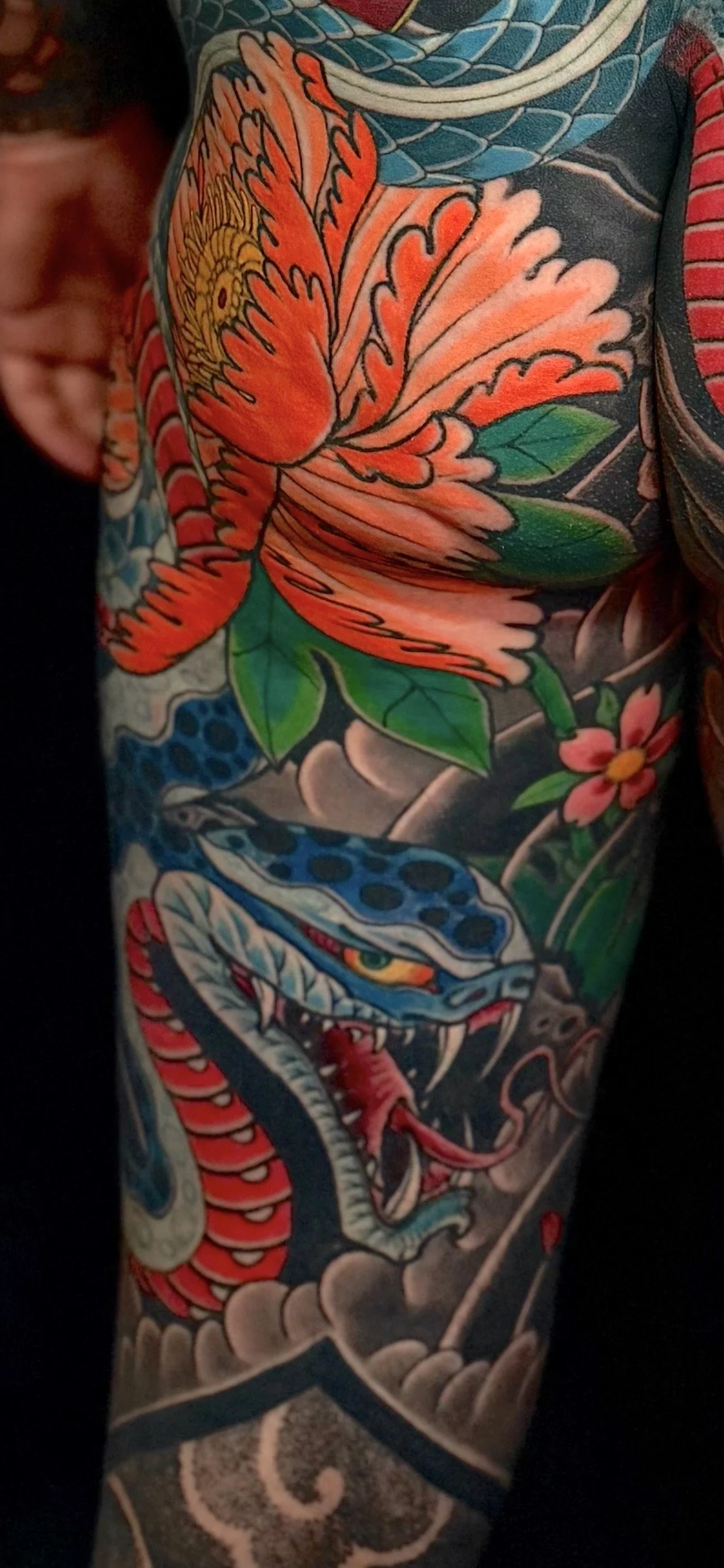 Brightly colored tattoo of a blue snake with red and yellow accents, intertwined with a large orange flower with green leaves.