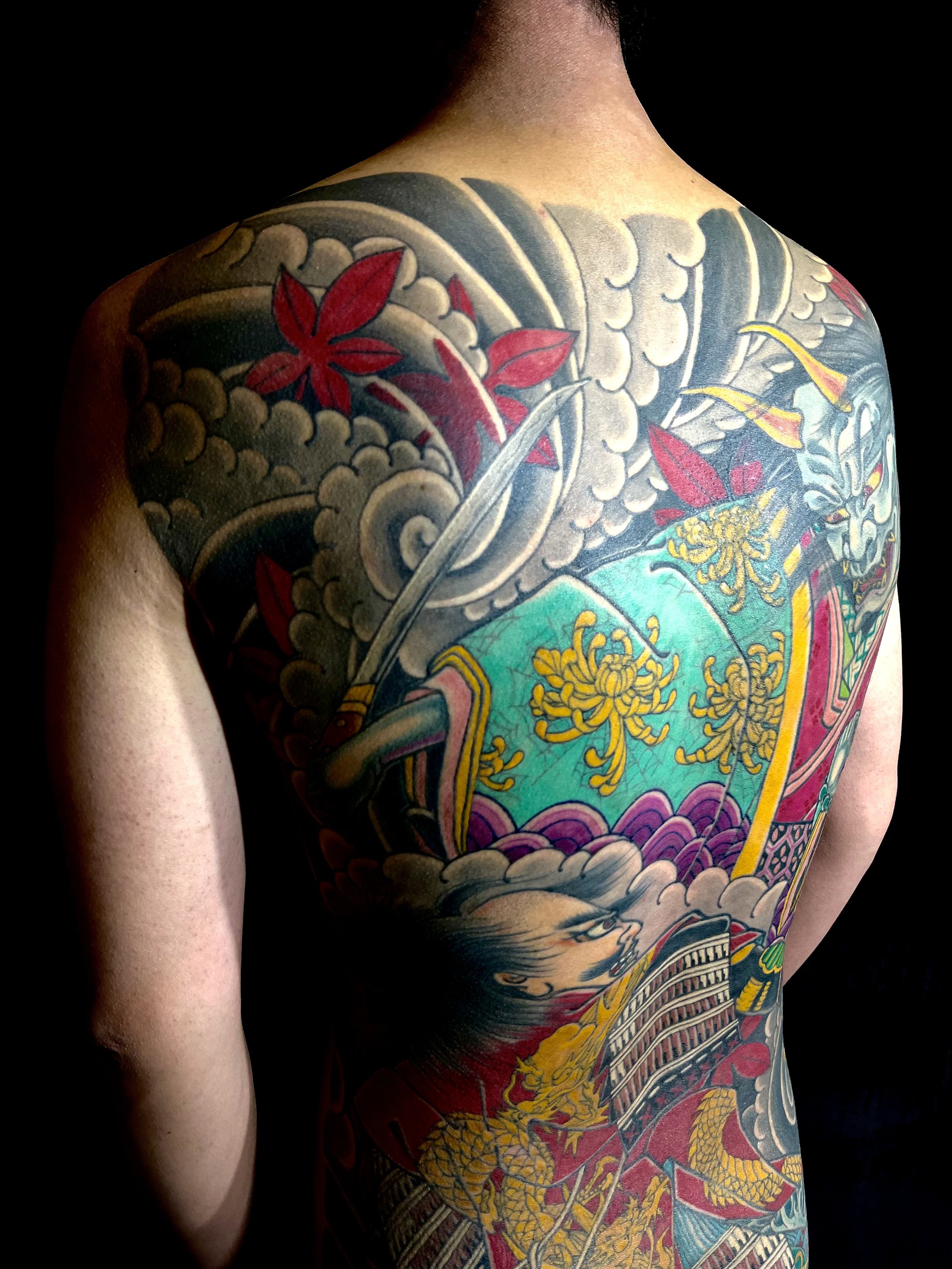 Colorful Japanese-style back tattoo featuring a samurai with a dragon, chrysanthemums, clouds, and traditional elements.