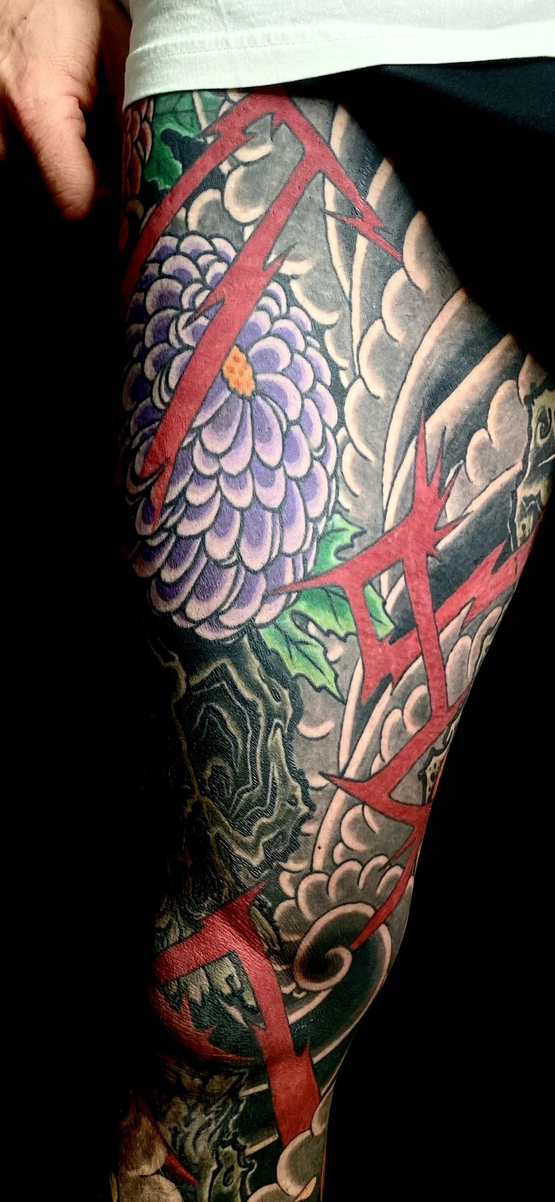 Close-up of a colorful tattoo sleeve featuring a purple chrysanthemum flower, green leaves, and red lightning bolt designs.
