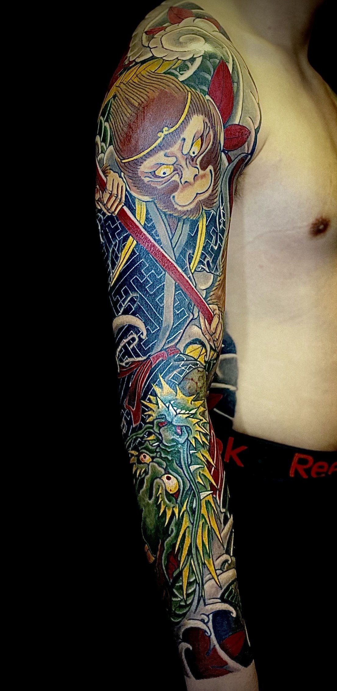 Colorful Japanese-style tattoo sleeve featuring a fierce warrior with a sword and a dragon.
