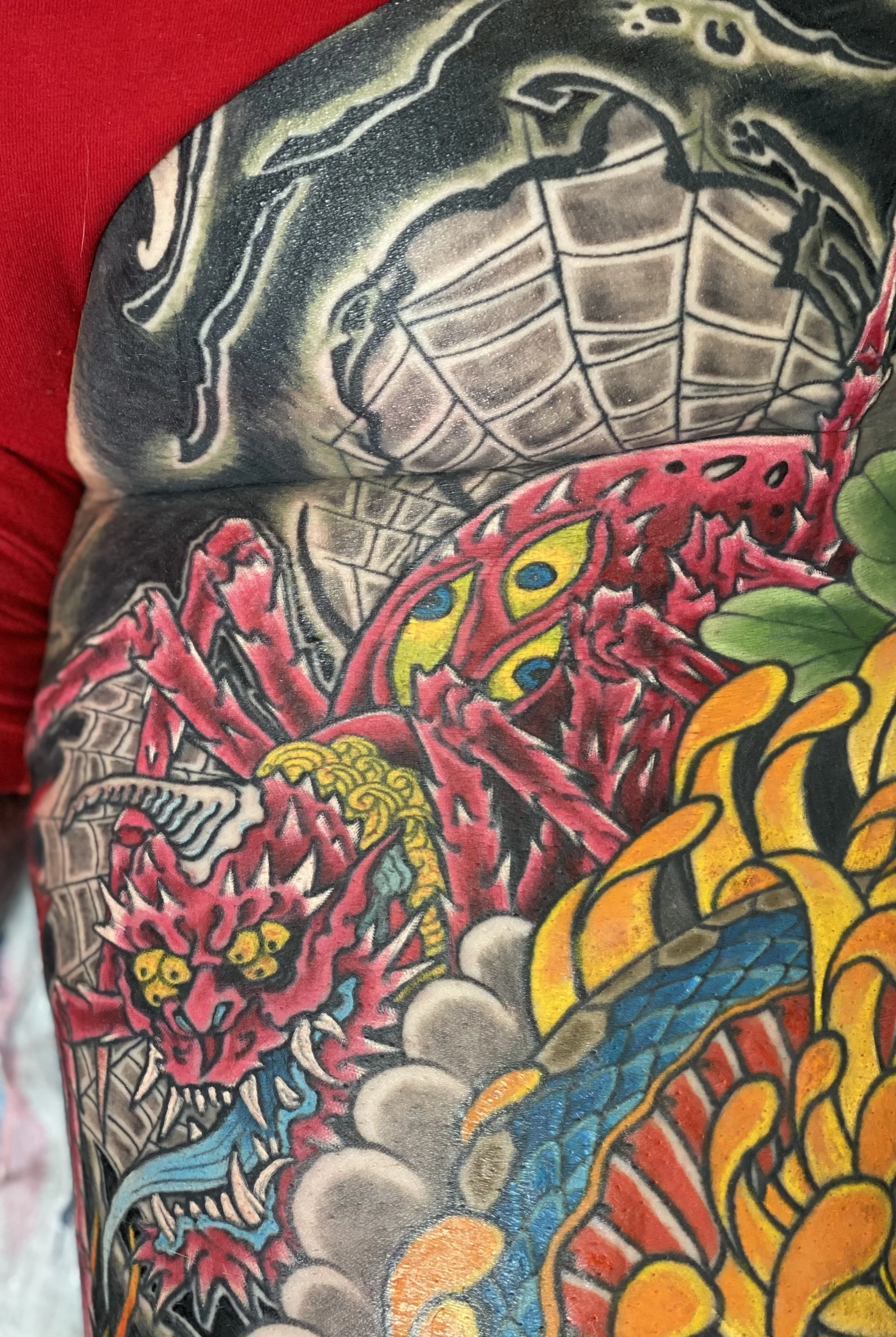 Close-up of a colorful tattoo sleeve featuring a green turtle, a pink crab with yellow and blue eyes, a fiery red dragon with blue eyes and sharp teeth, smoke, and flames.