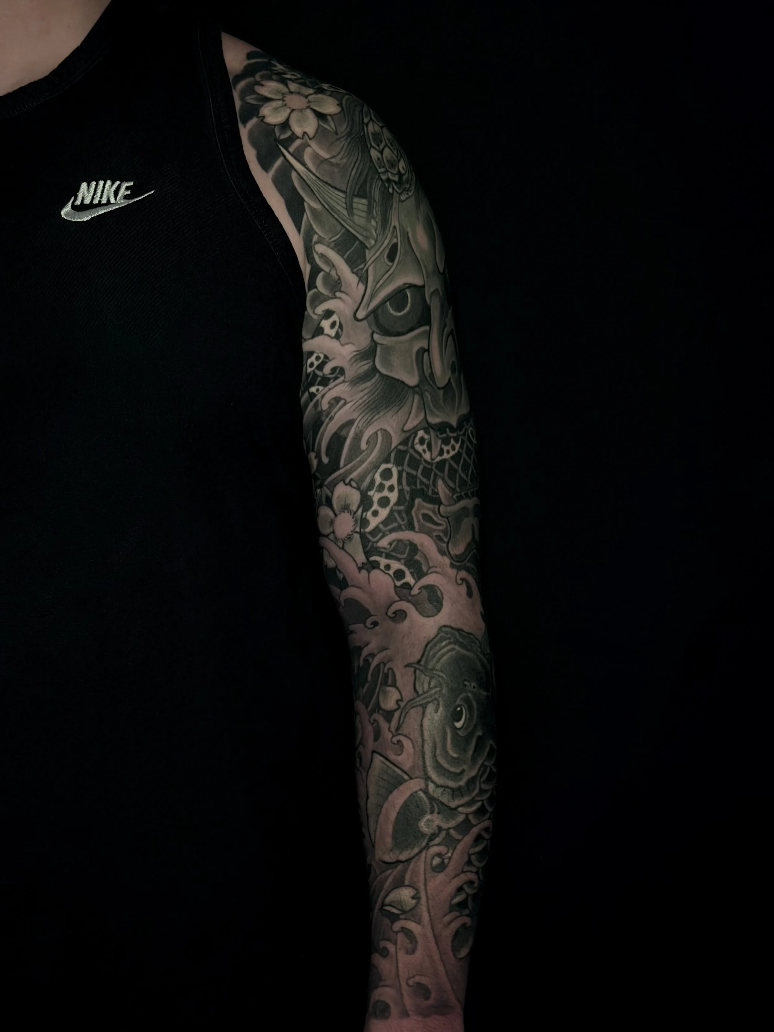 Close-up of a tattooed arm with Japanese-style dragon design on a person wearing a black Nike shirt.