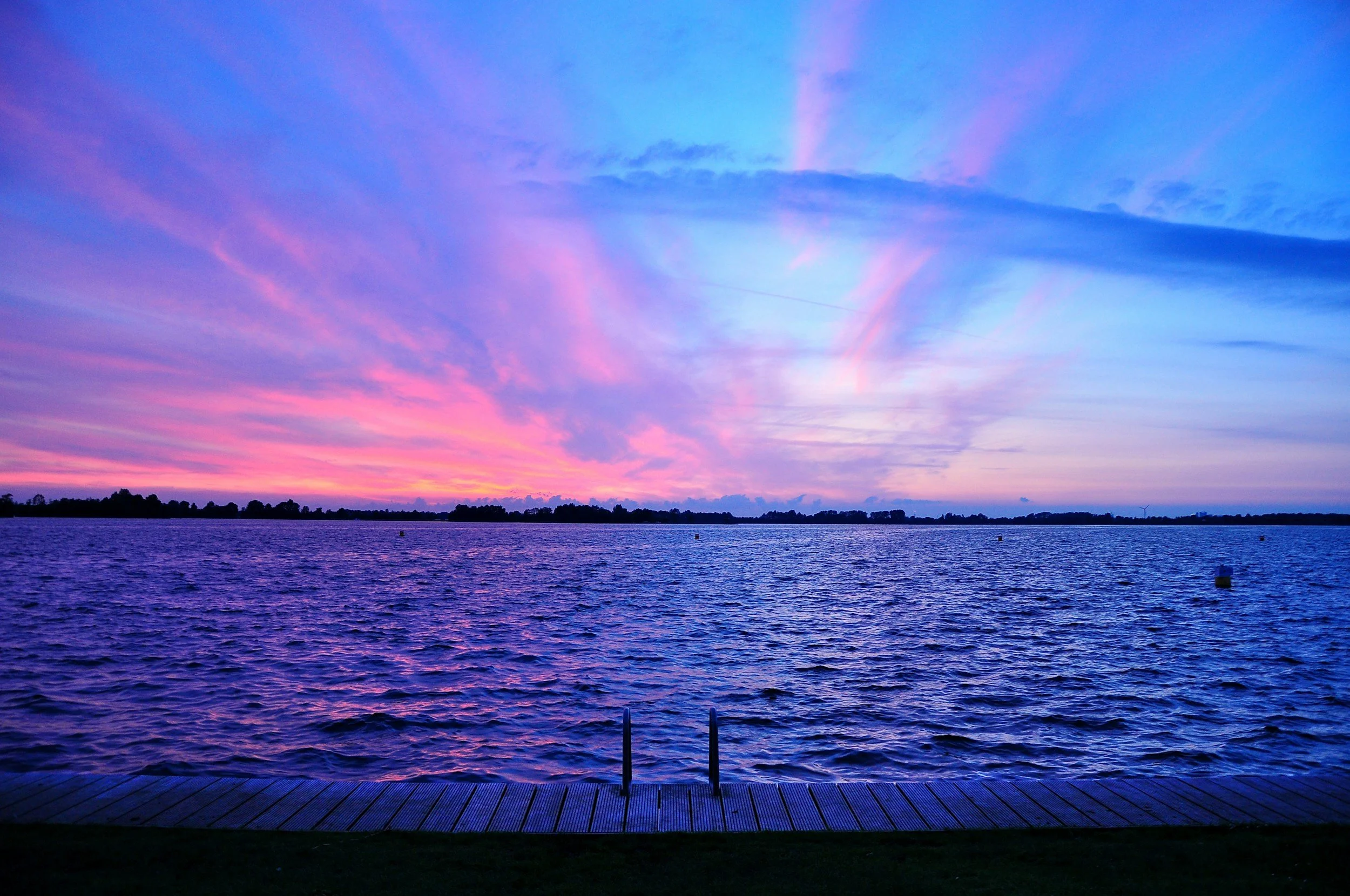 Sunset over a body of water with a dock in the foreground and colorful clouds in the sky.