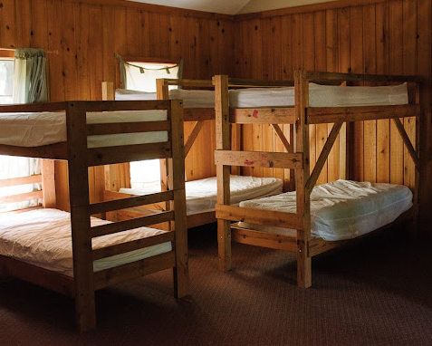 A room with wooden walls and three wooden bunk beds with mattresses, pillows, and blankets.