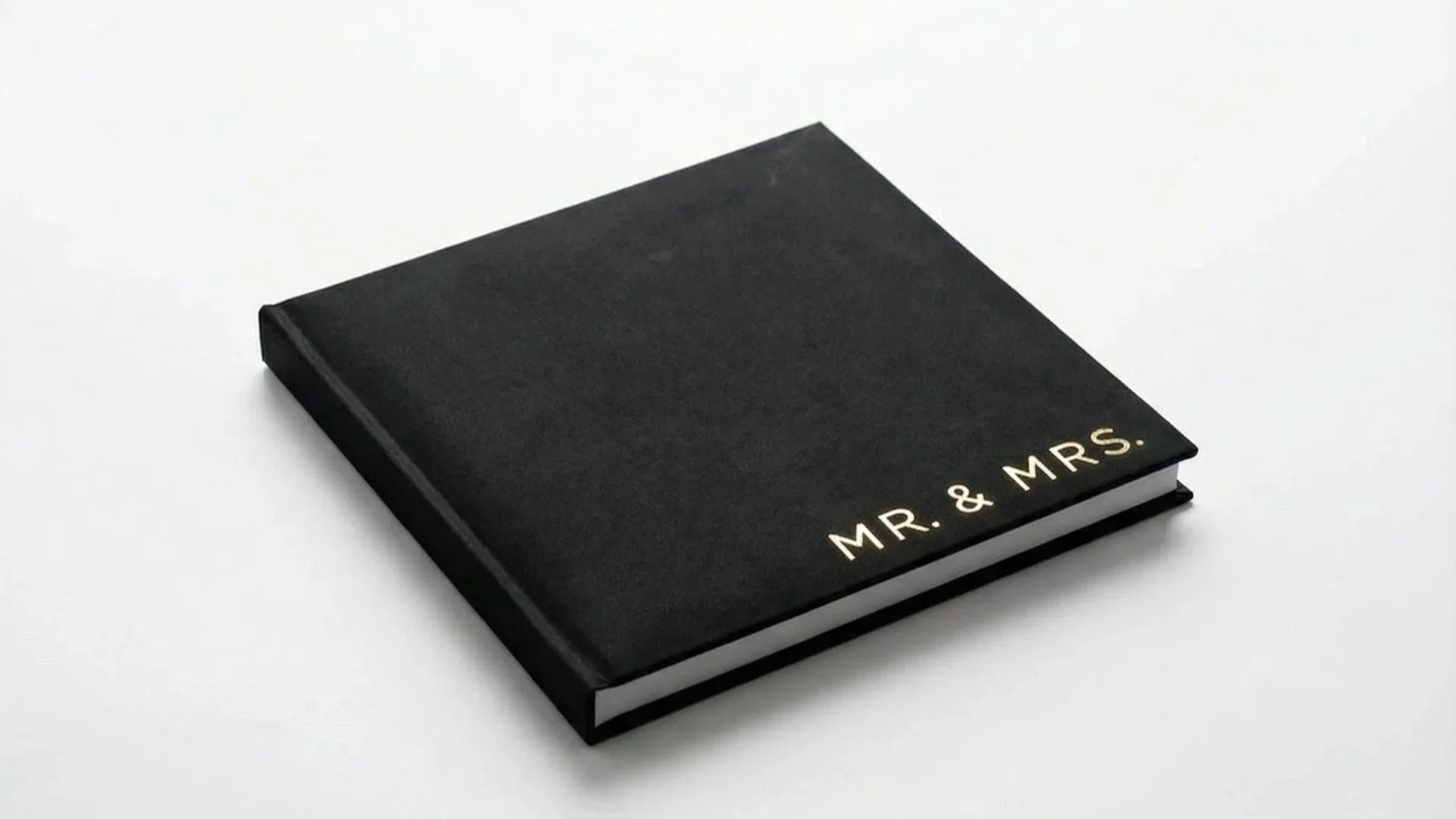 Black photo album with gold lettering that says "MR. & MRS." on the bottom right corner, placed on a white background.