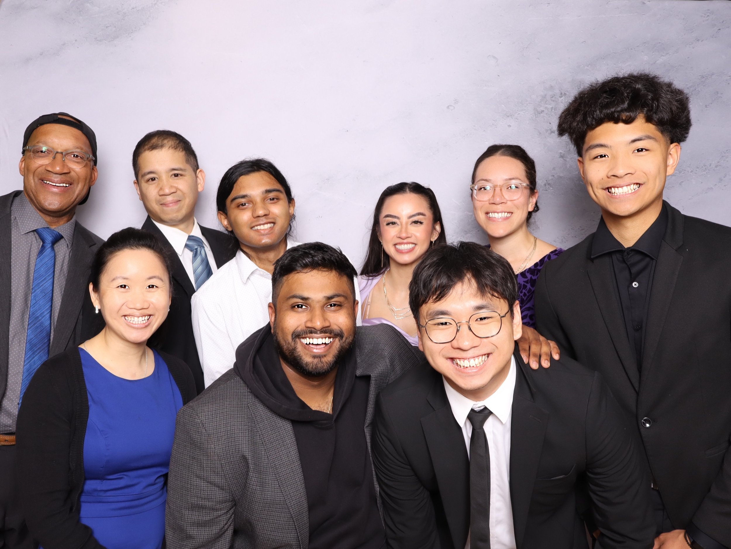 Group photo of ten diverse smiling professionals in business attire posing against a gray backdrop.