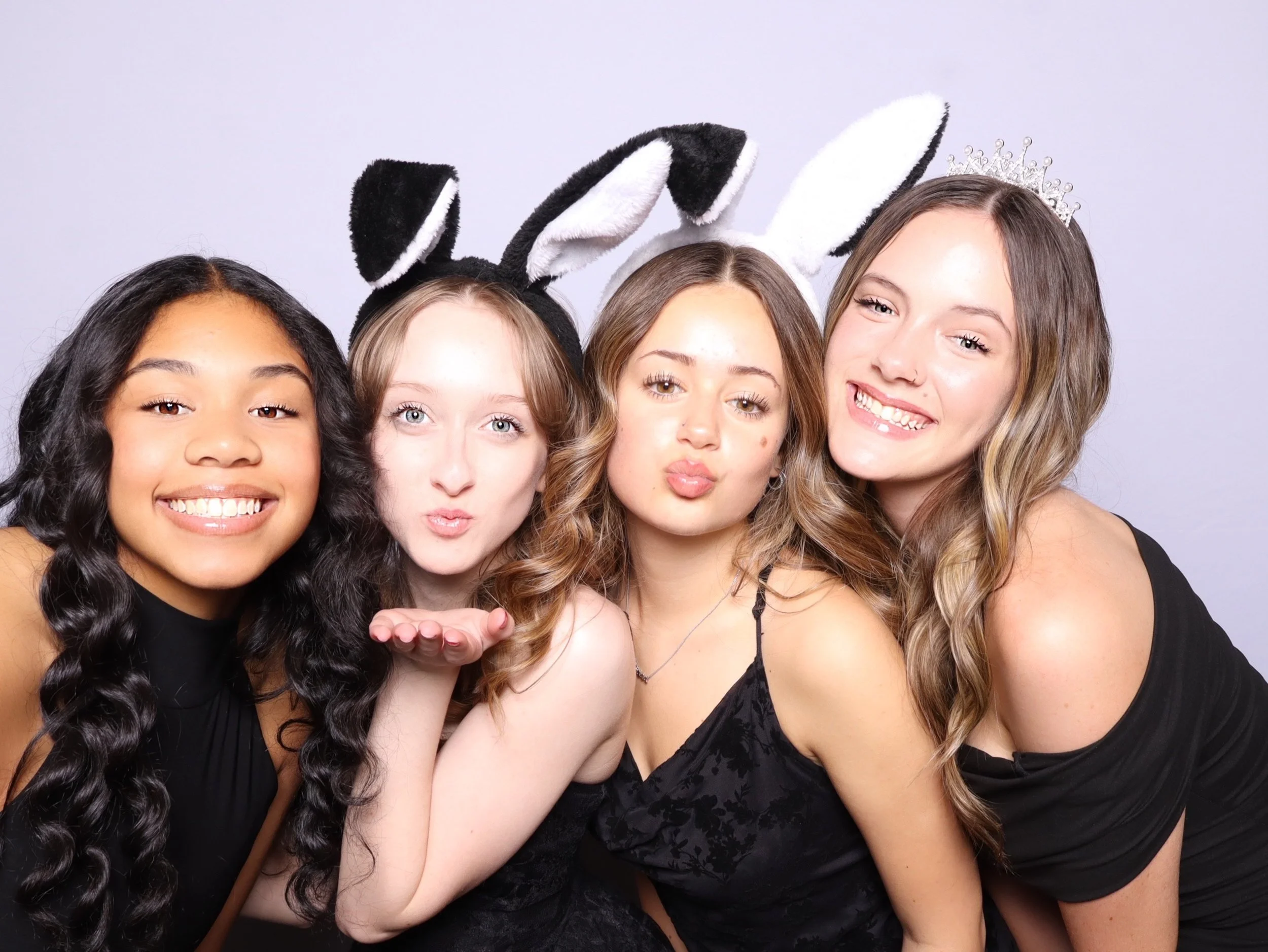 Four smiling young women posing together in a photo booth, wearing bunny ears and a tiara.