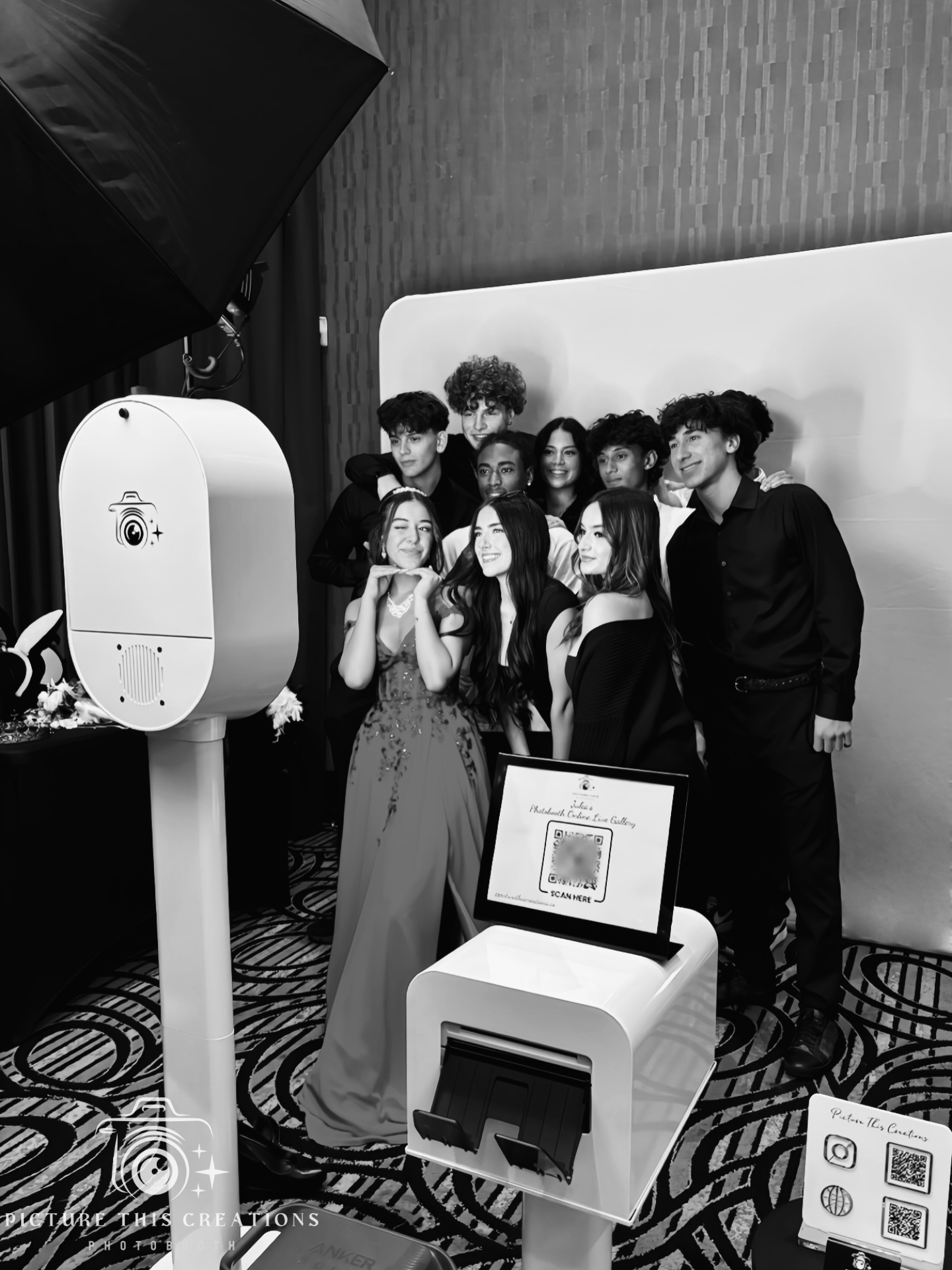 A group of young people posing for a photo in a photo booth, with a photographer's studio setup, including a large softbox light and a camera icon on the photo booth screen.