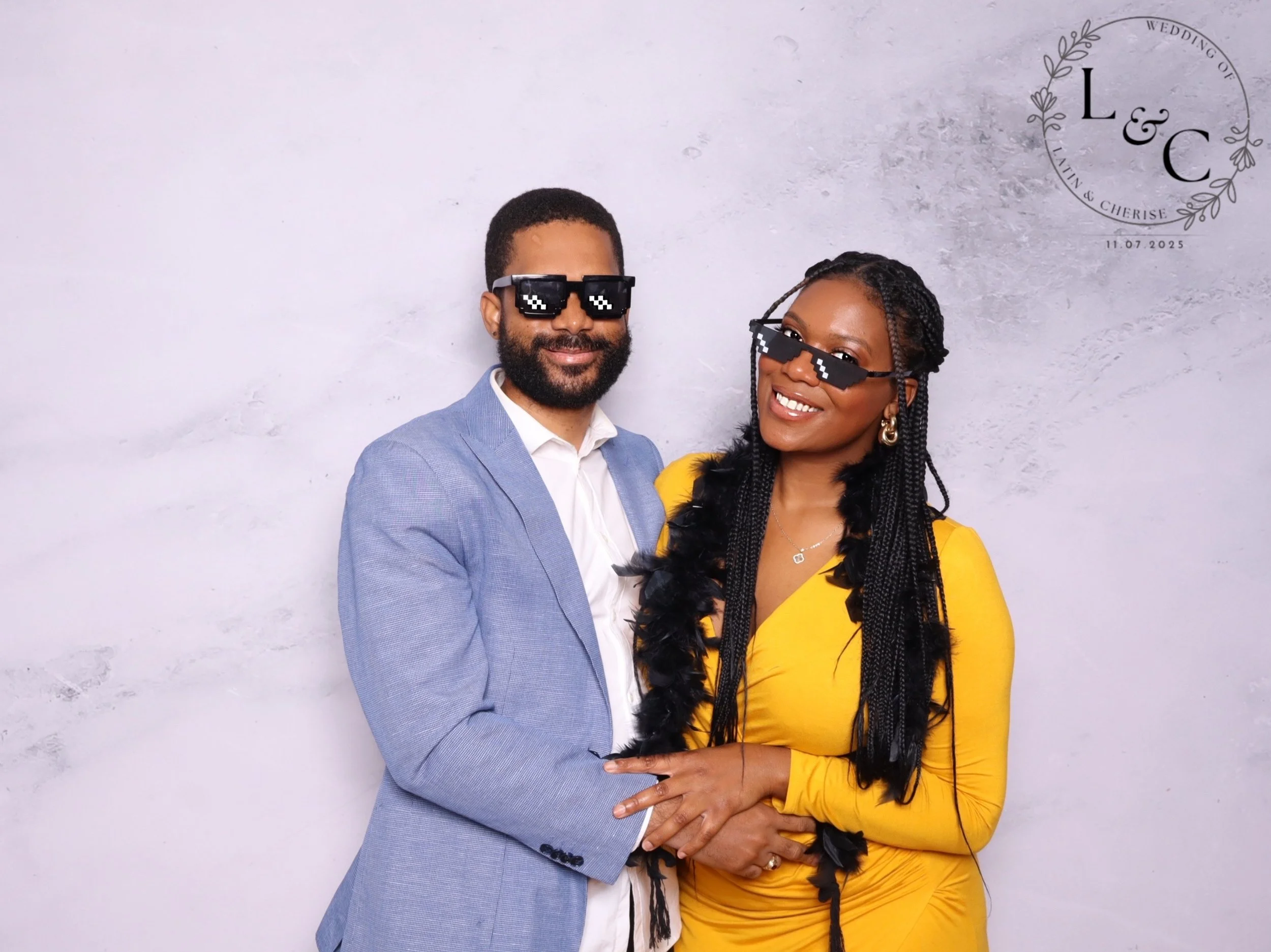 A couple dressed in formal attire at a wedding, wearing pixelated sunglasses, standing close together with the man holding the woman’s hand, against a gray background with wedding details to the upper right.