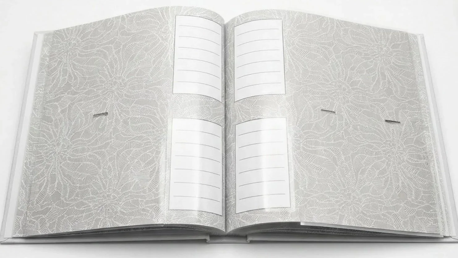 An open book with floral patterned pages, featuring four white rectangular sections with horizontal lines for text, on a white surface.