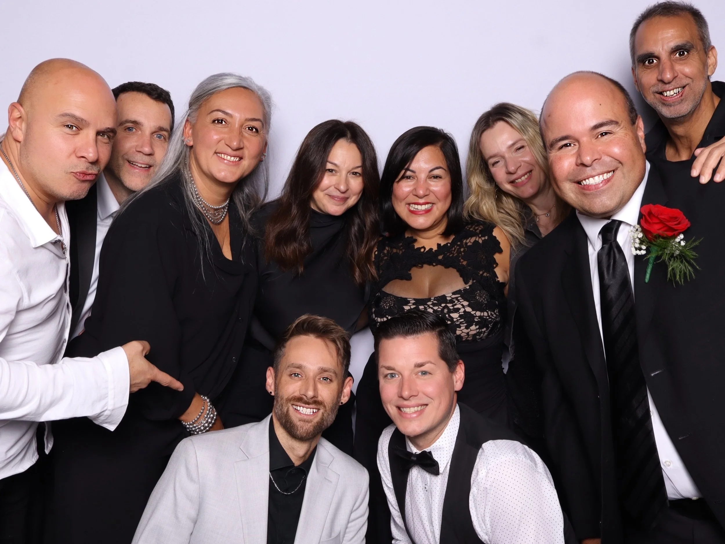 Group of ten people dressed in formal attire, smiling at the camera, with a plain white backdrop.