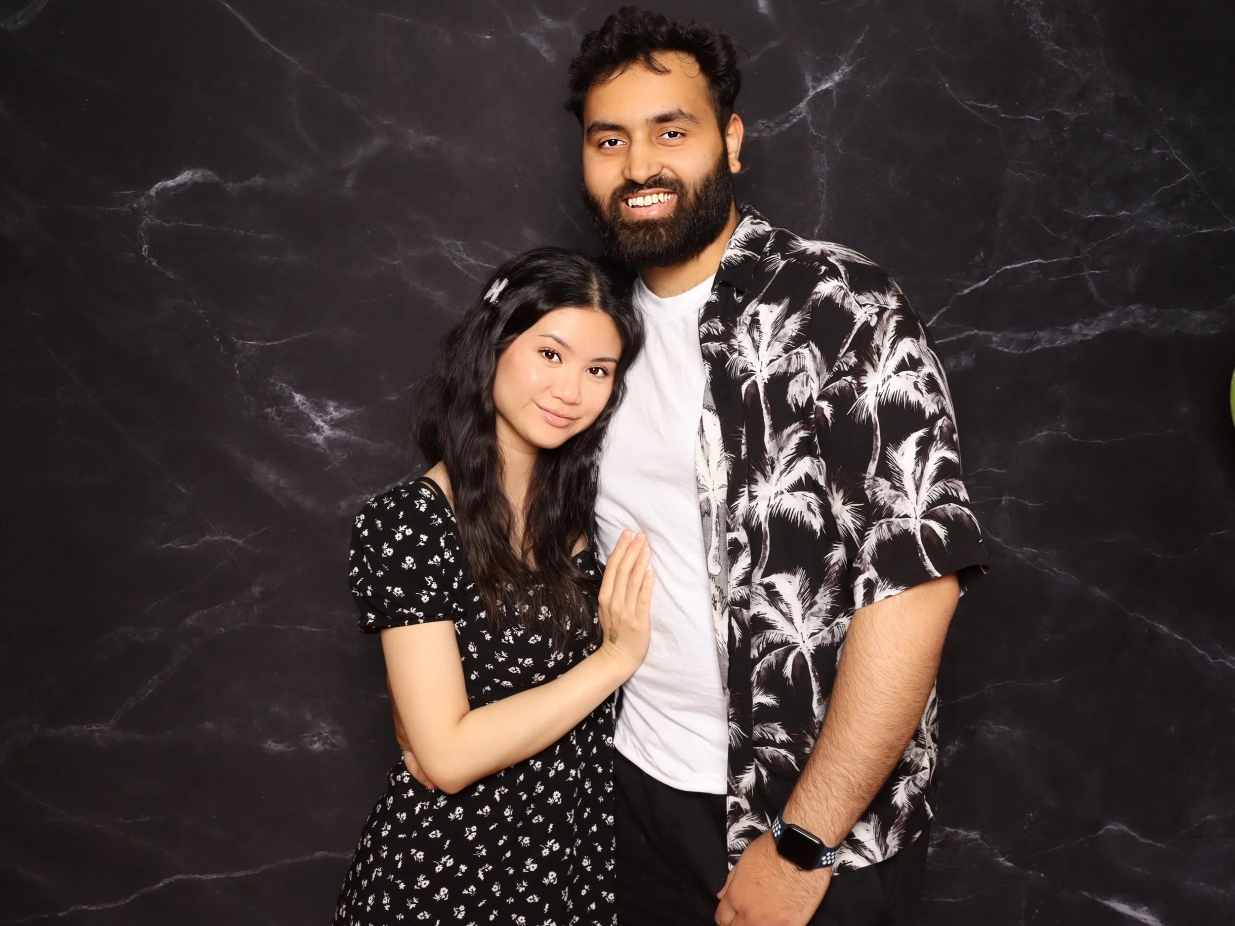 A young woman and a young man standing close together against a dark marbled background, smiling, with the woman touching the man's chest.