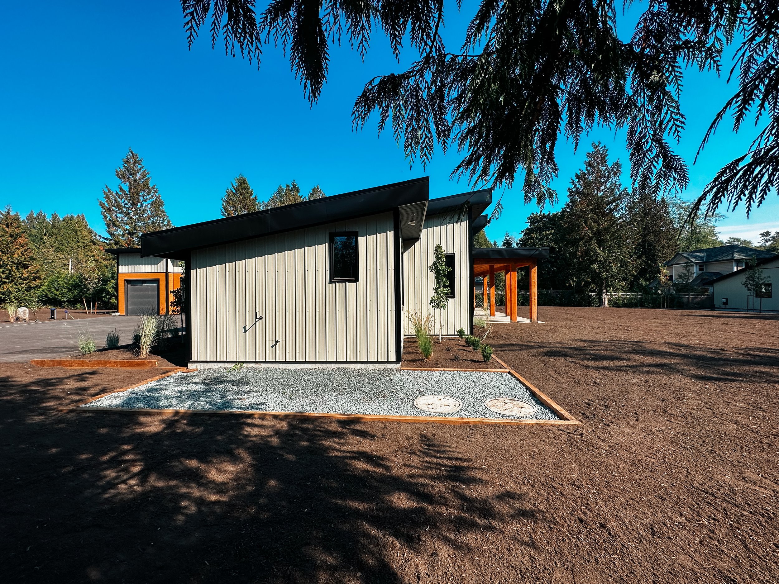 Modern house with metal siding, gravel landscaping, and wooden accents, surrounded by trees.