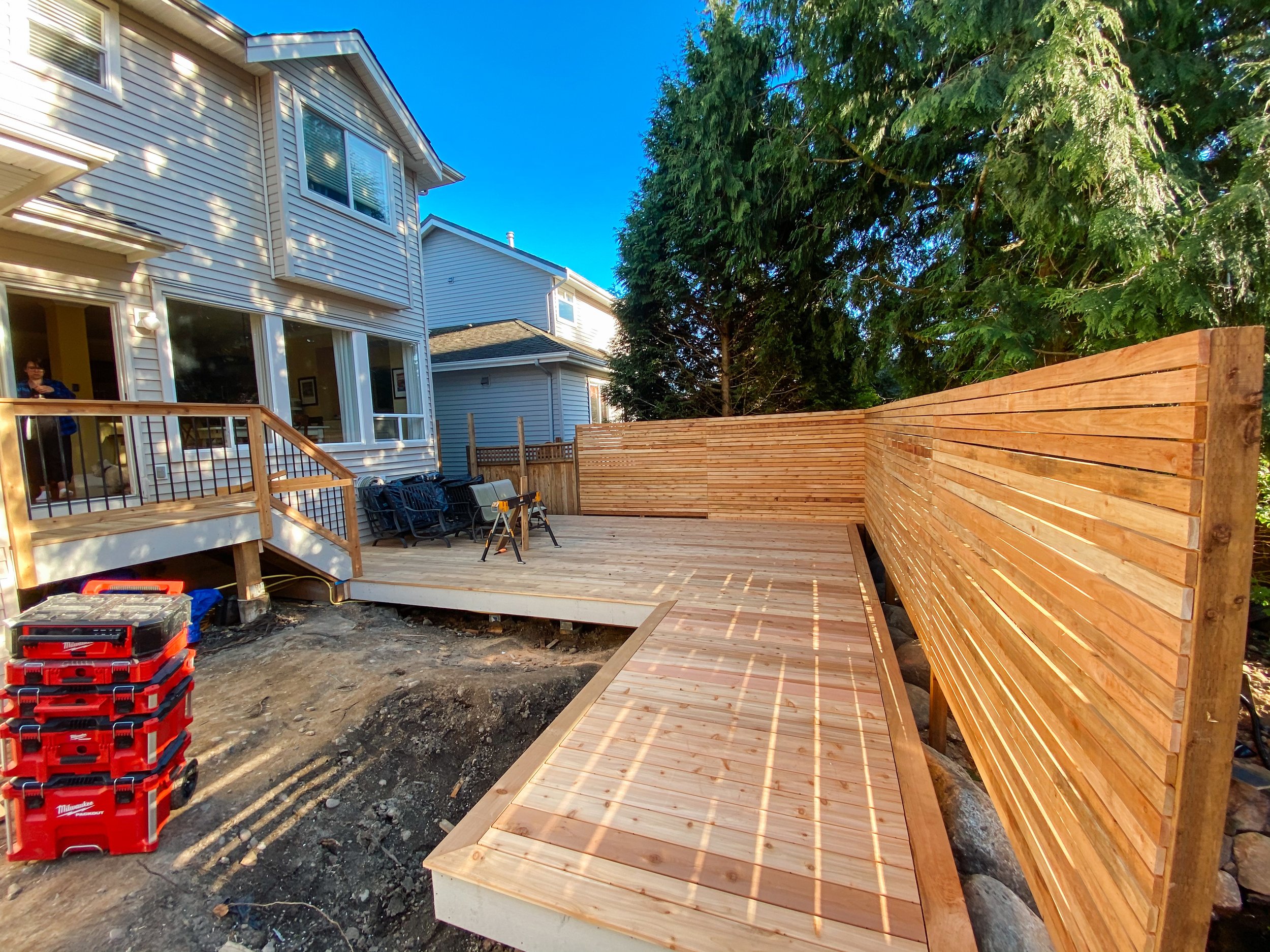 Wooden deck under construction, with a tall privacy fence and adjoining two-story house.