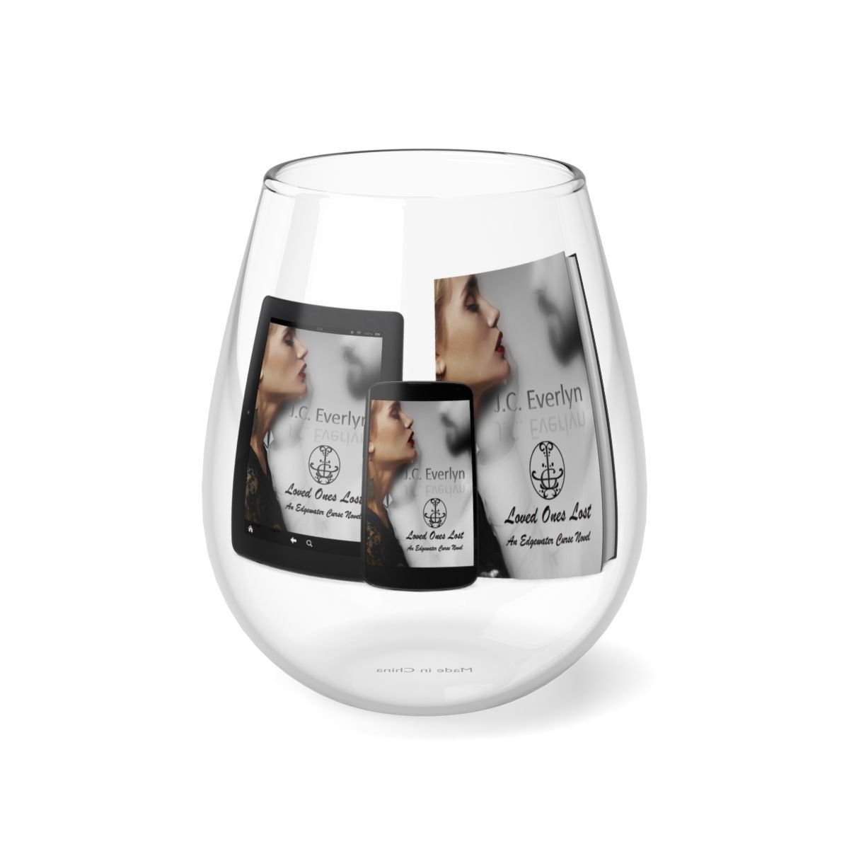 A clear glass with printed images of a woman, a tablet, and a phone showing a book cover titled "Loved Ones Lost" by J.C. Everlyn, inside the glass.
