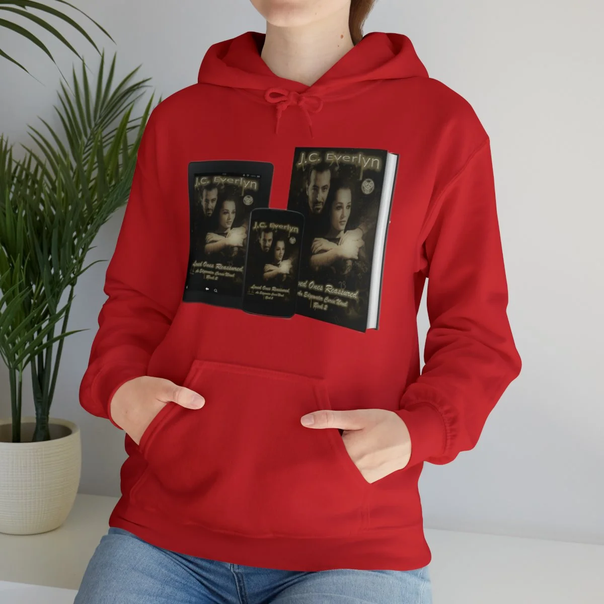 Person wearing a red hoodie with images of a book cover titled 'J.C. Evelyn' displayed on it, with the person’s hand in the hoodie pocket and a plant in the background.