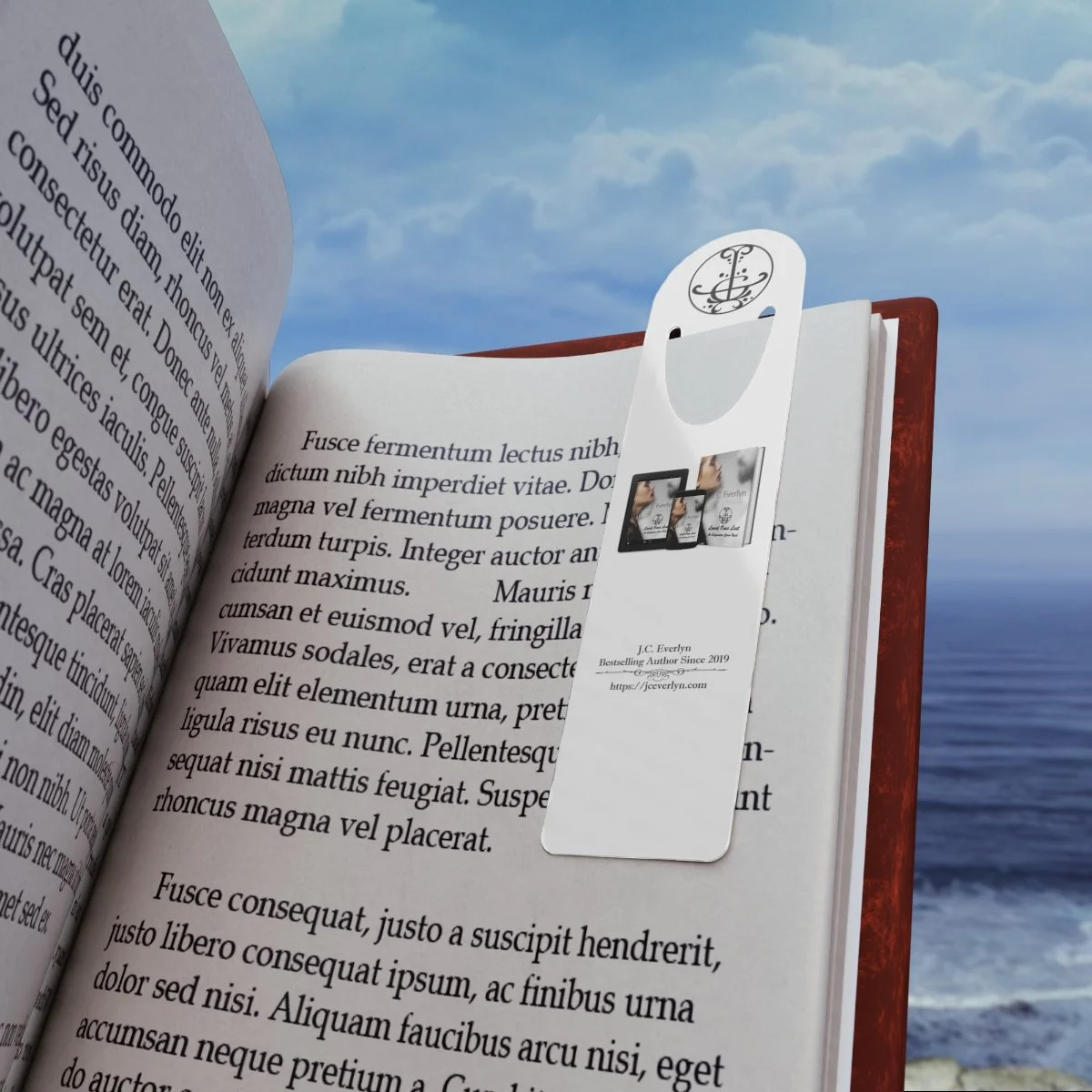 An open book with a paper bookmark standing up on the right page, with a cloudy sky and ocean in the background.