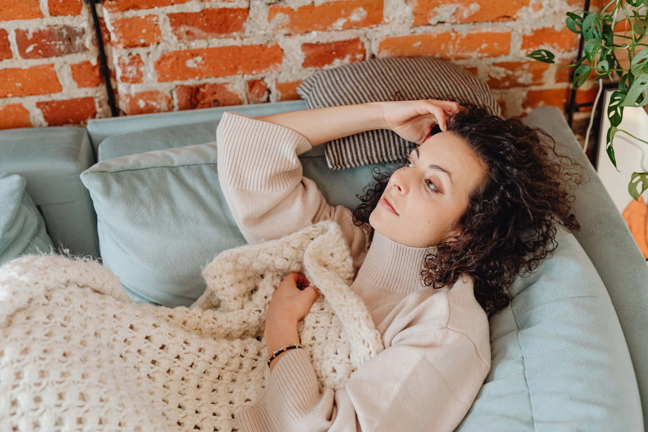 Woman lying on a couch with eyes open, unable to fully rest, representing how the mental load keeps the nervous system in a low-grade state of alert