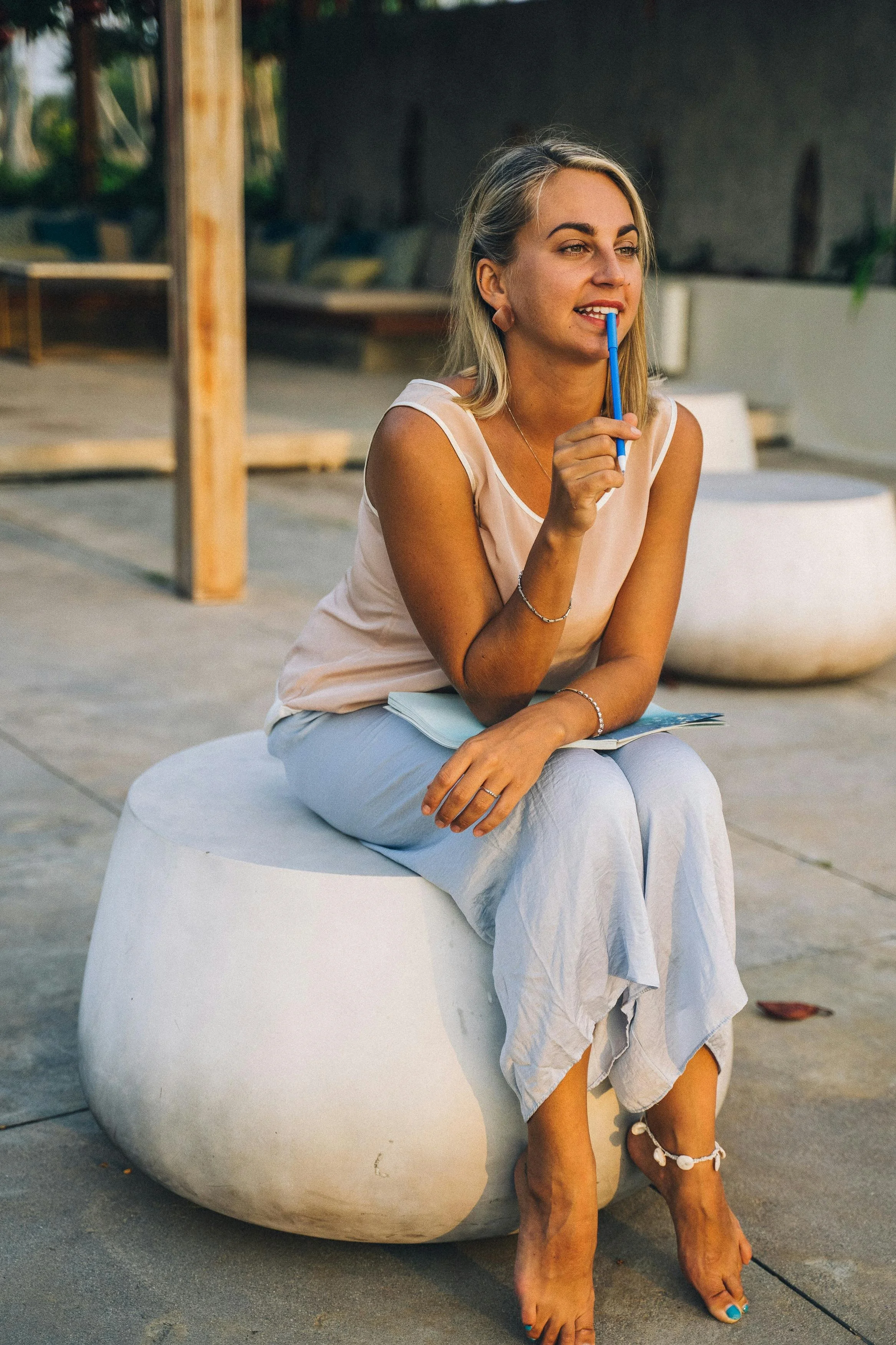 Woman sitting outdoors holding a pen thoughtfully, looking reflective — therapy for boundaries and self-trust