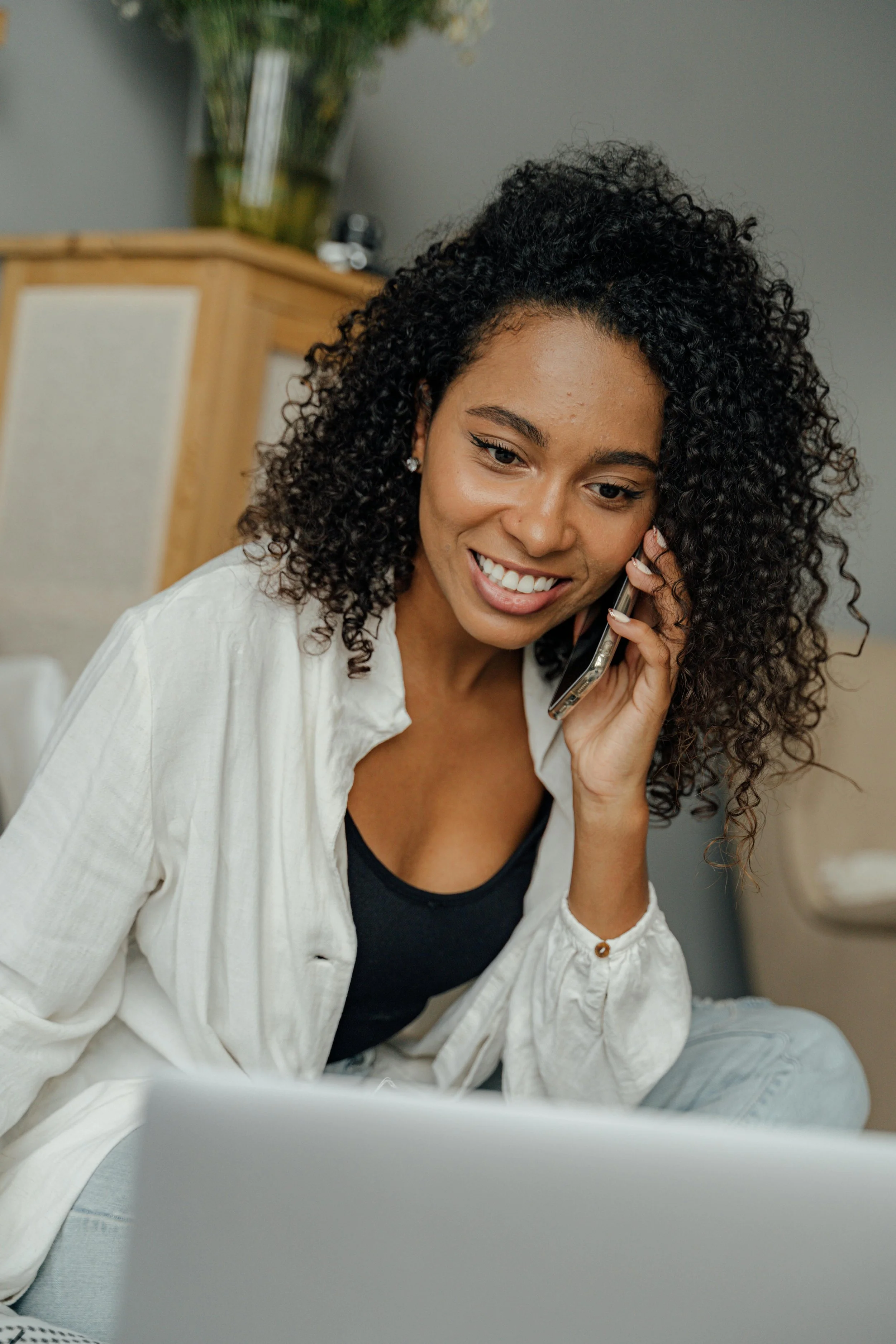 A woman smiling softly while talking on her phone, representing the comfort and connection of reaching out for online therapy with Erin Reddinger.