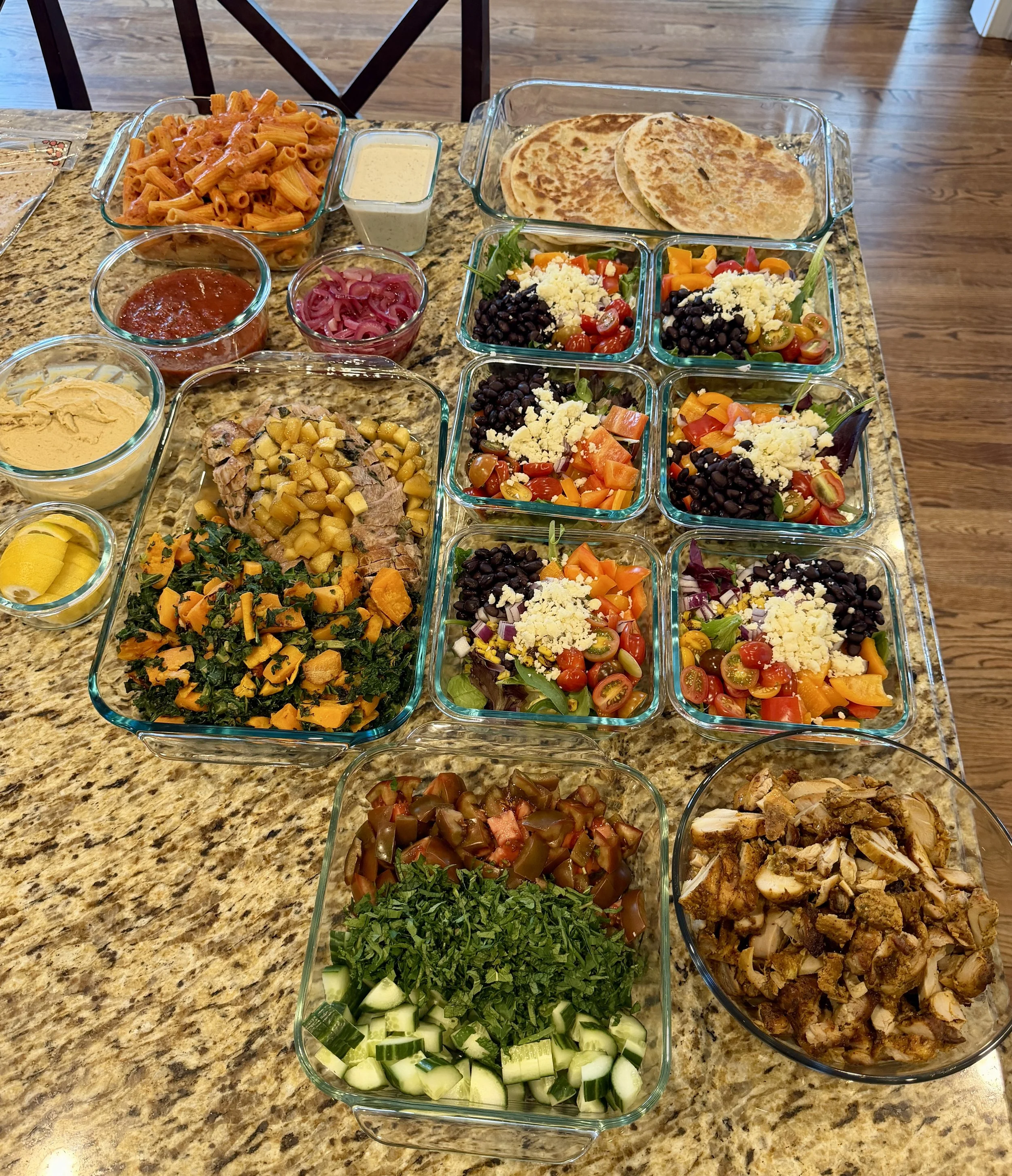 Assorted dishes on a kitchen counter including pasta, tortillas, salads with vegetables, cheese, and beans, along with sauces and cooked meats.