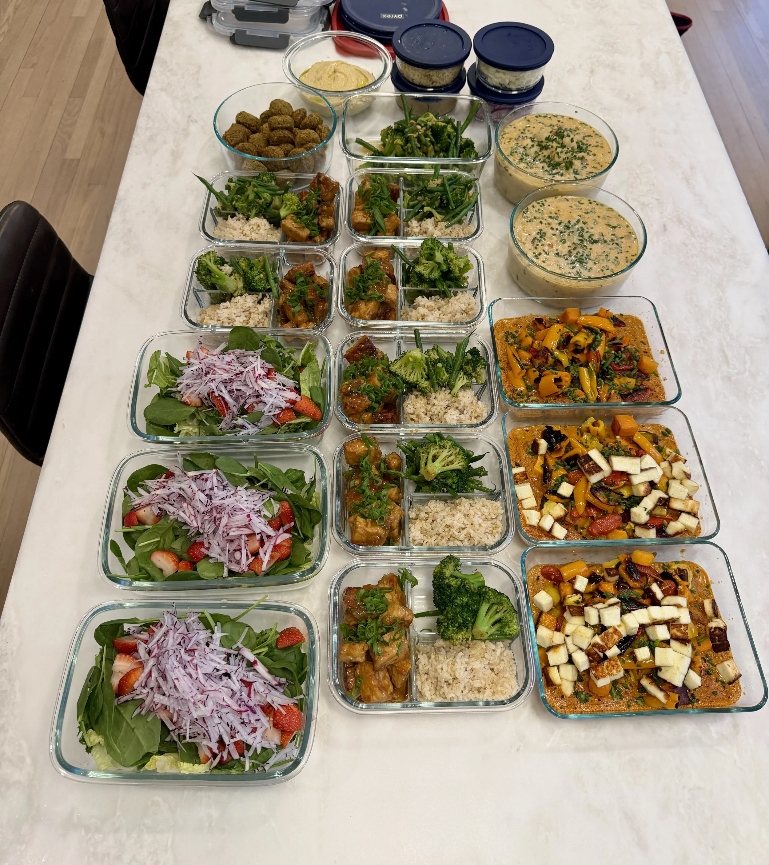 Assorted prepared food dishes on a white table, including salads, rice, vegetable stews, and dips in glass containers.