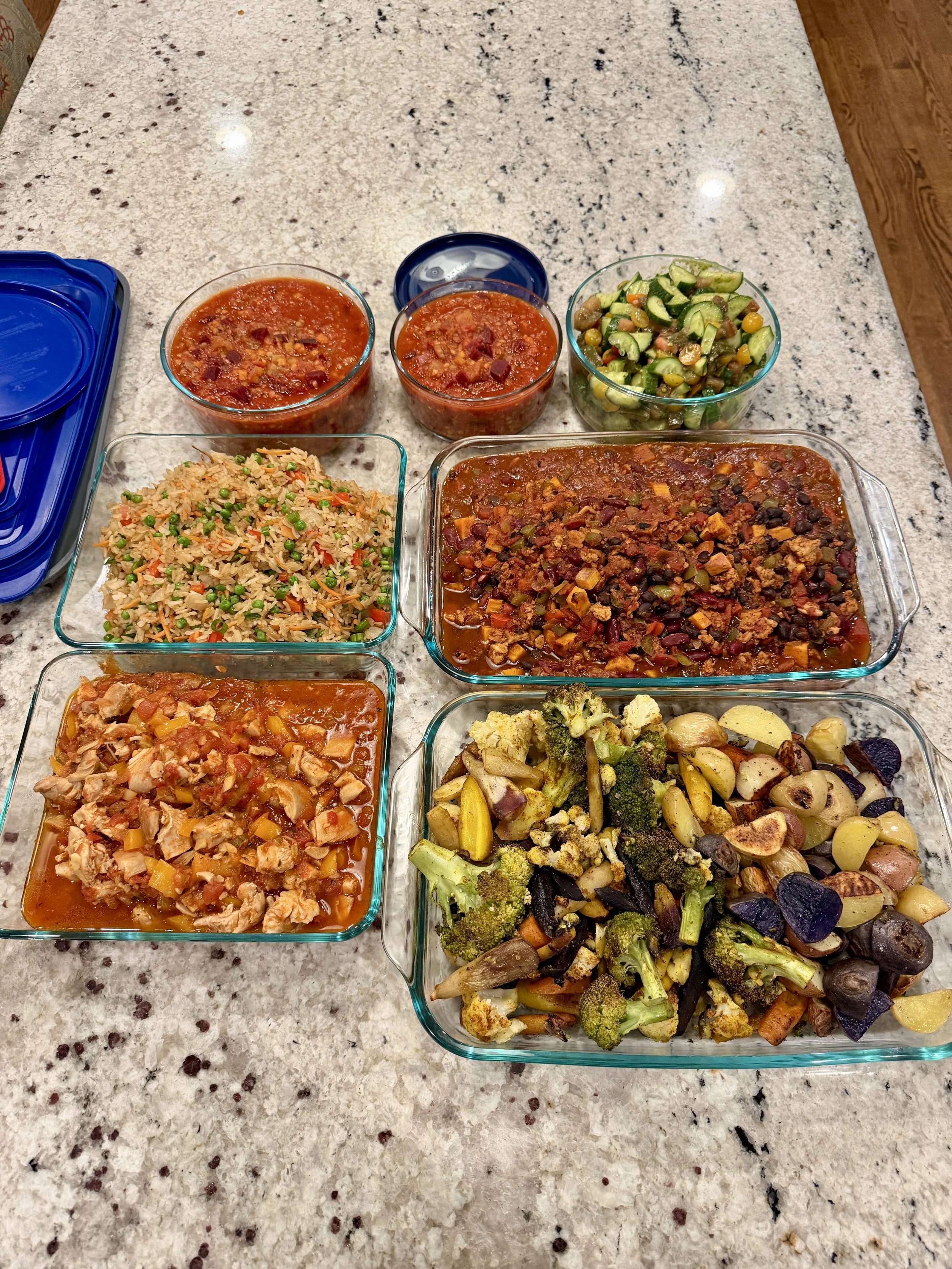Various dishes of Mexican food on a kitchen countertop, including rice with vegetables, chili with meat, vegetable salad, and roasted vegetables in glass dishes.