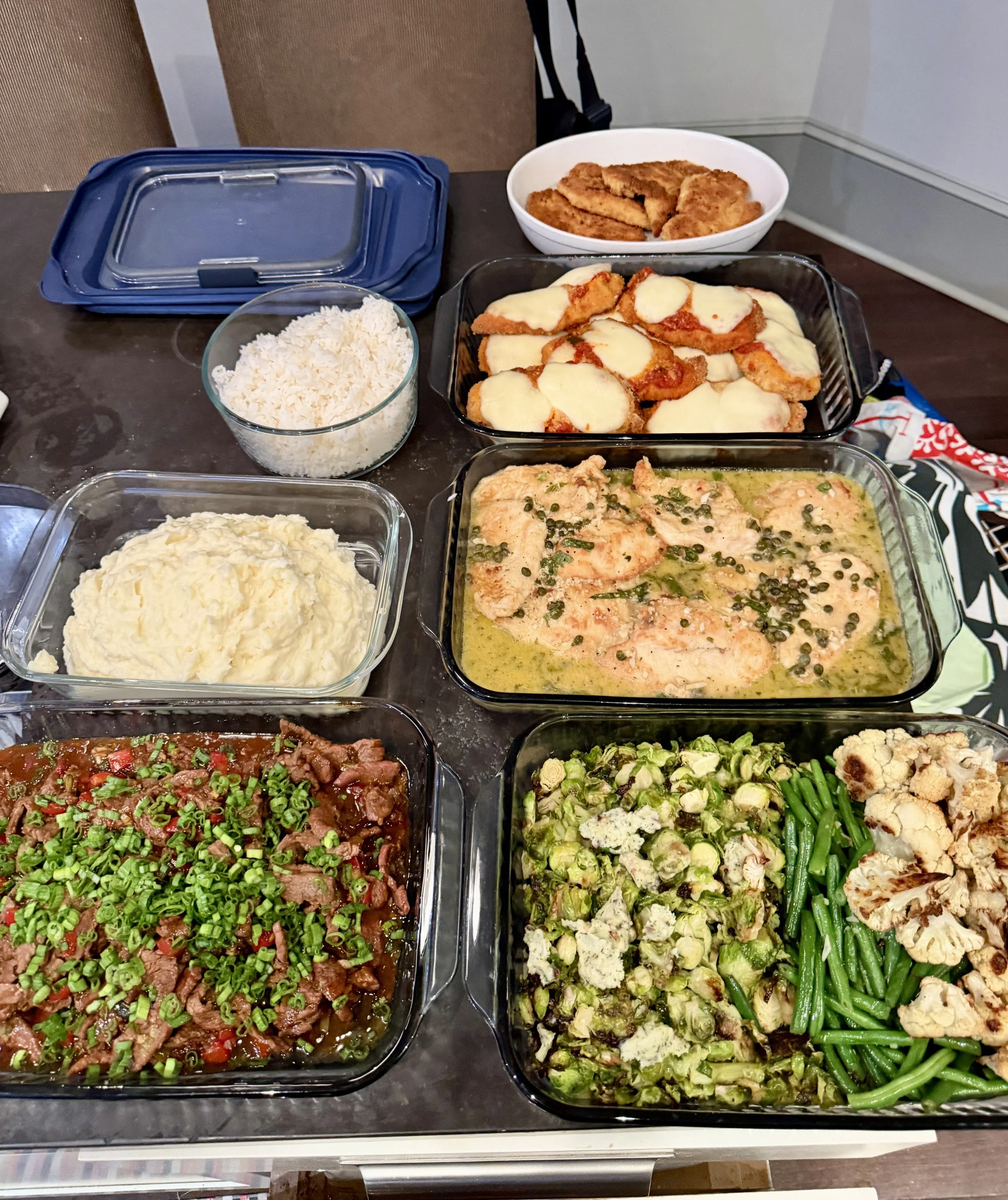 A table of various prepared dishes including mashed potatoes, rice, fried chicken with mozzarella, chicken in cream sauce with capers, beef stew with vegetables, roasted brussels sprouts, cauliflower, and green beans.