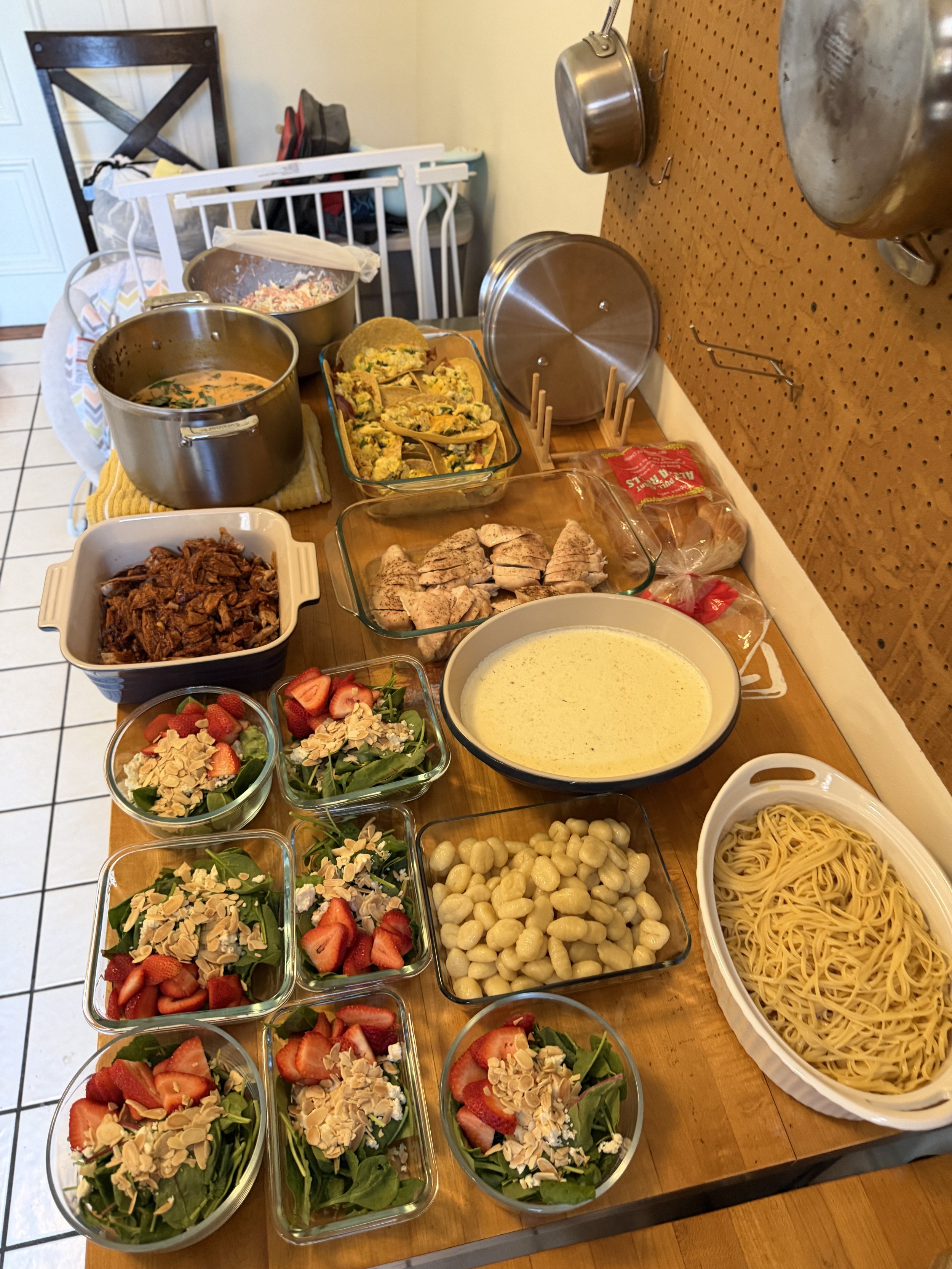 A dining table with various food dishes, including salads with strawberries and almonds, cooked chicken, pasta, and bowls of soup or sauce, arranged for a meal.