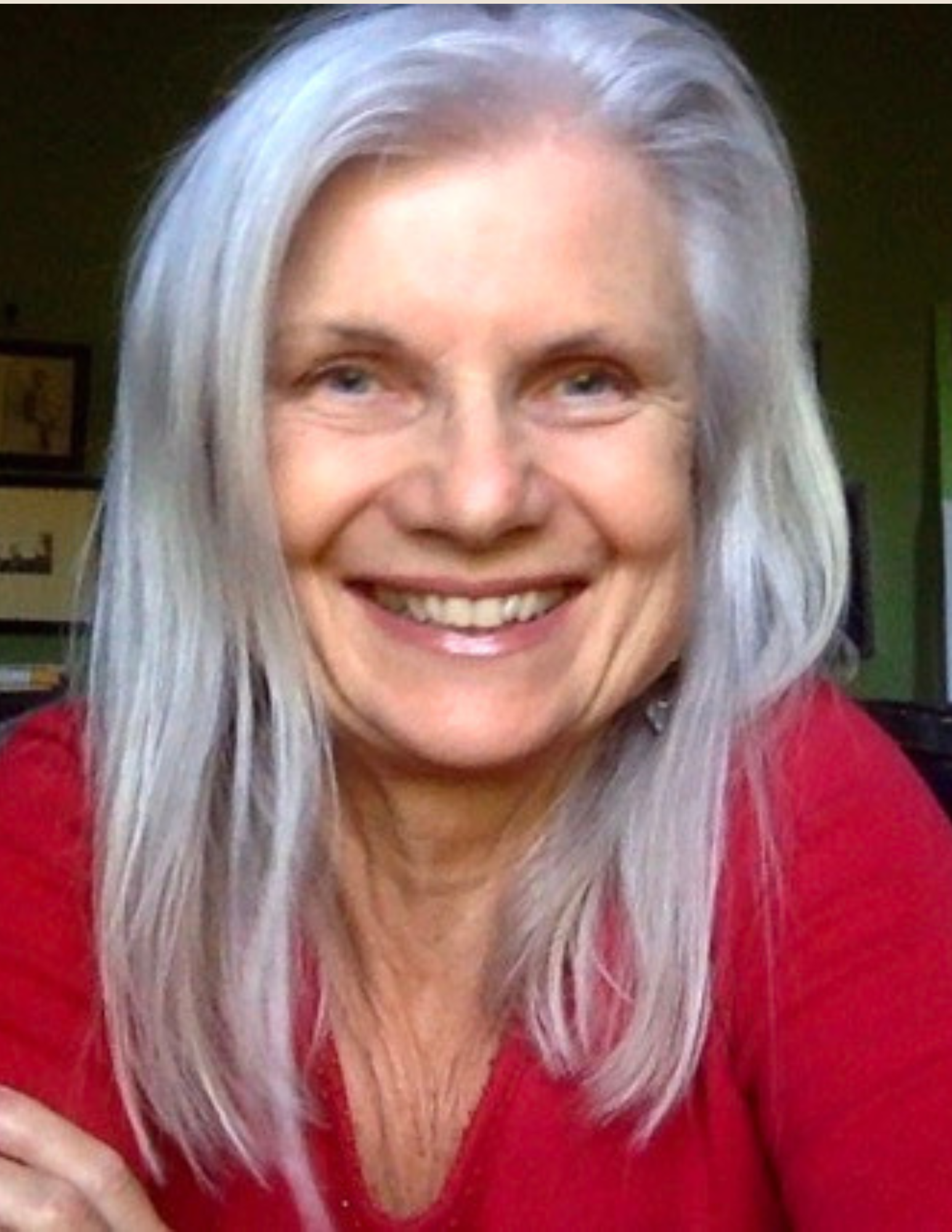 Smiling person with long gray hair wearing a red sweater, indoors.