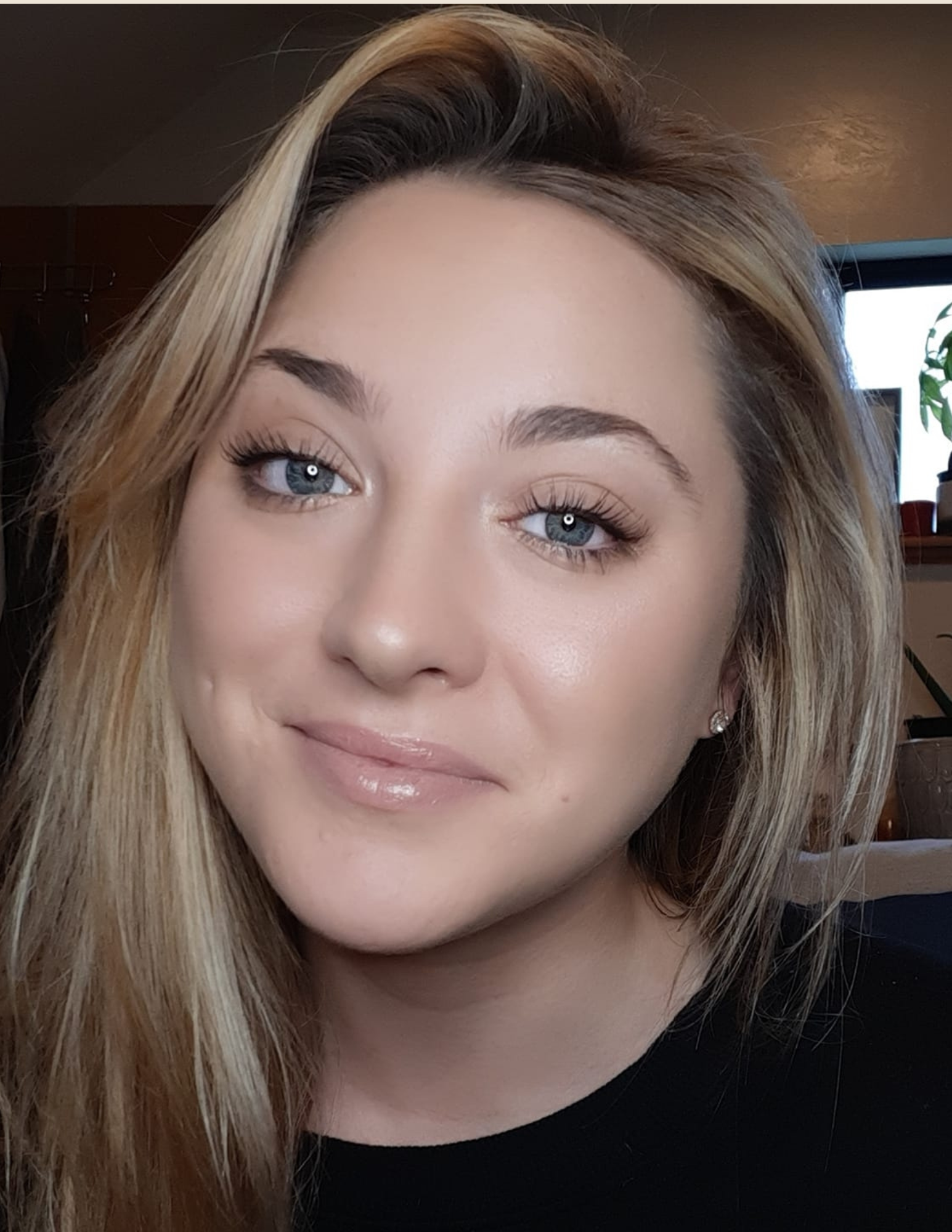 Person with long blonde hair and blue eyes smiling indoors
