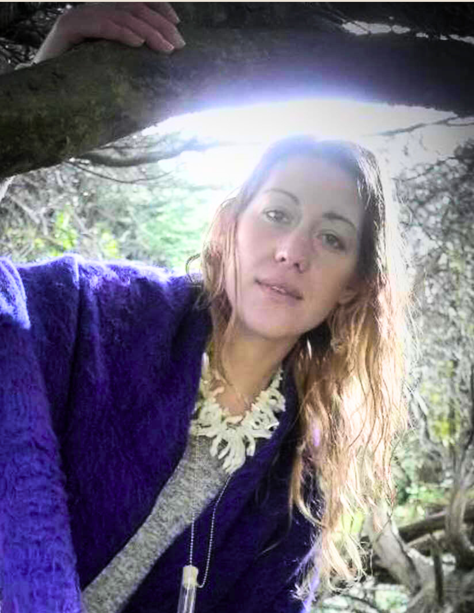 Woman wearing a purple coat in a forest setting, leaning on a tree branch.