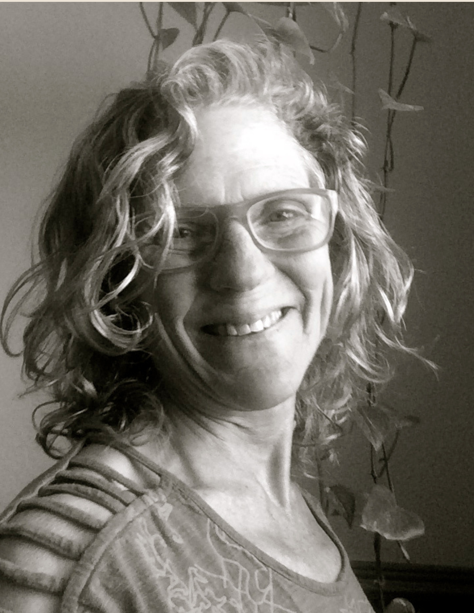 Smiling person with curly hair and glasses in a black-and-white photo.