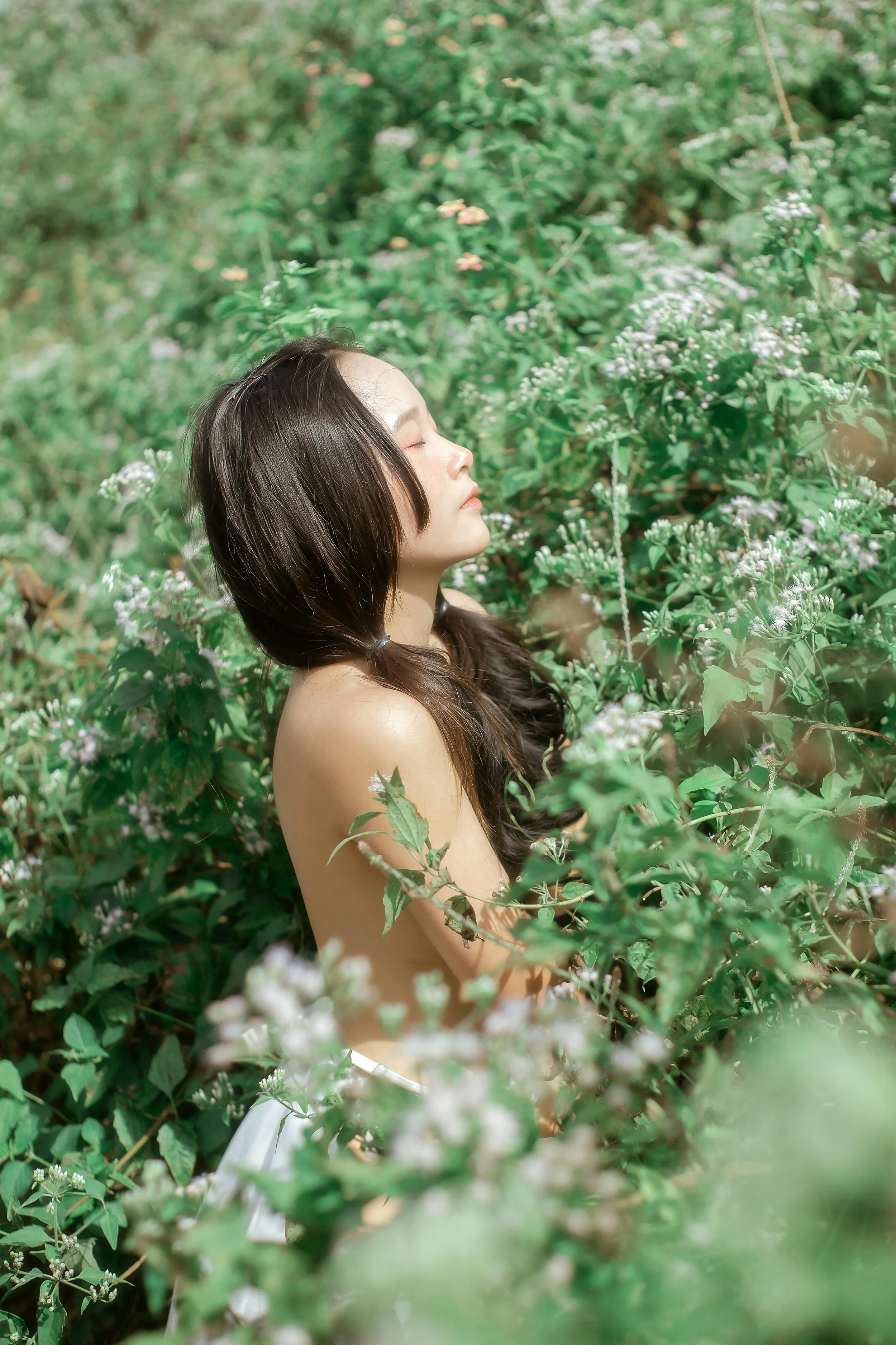 Young woman with closed eyes in a field of greenery and small flowers.