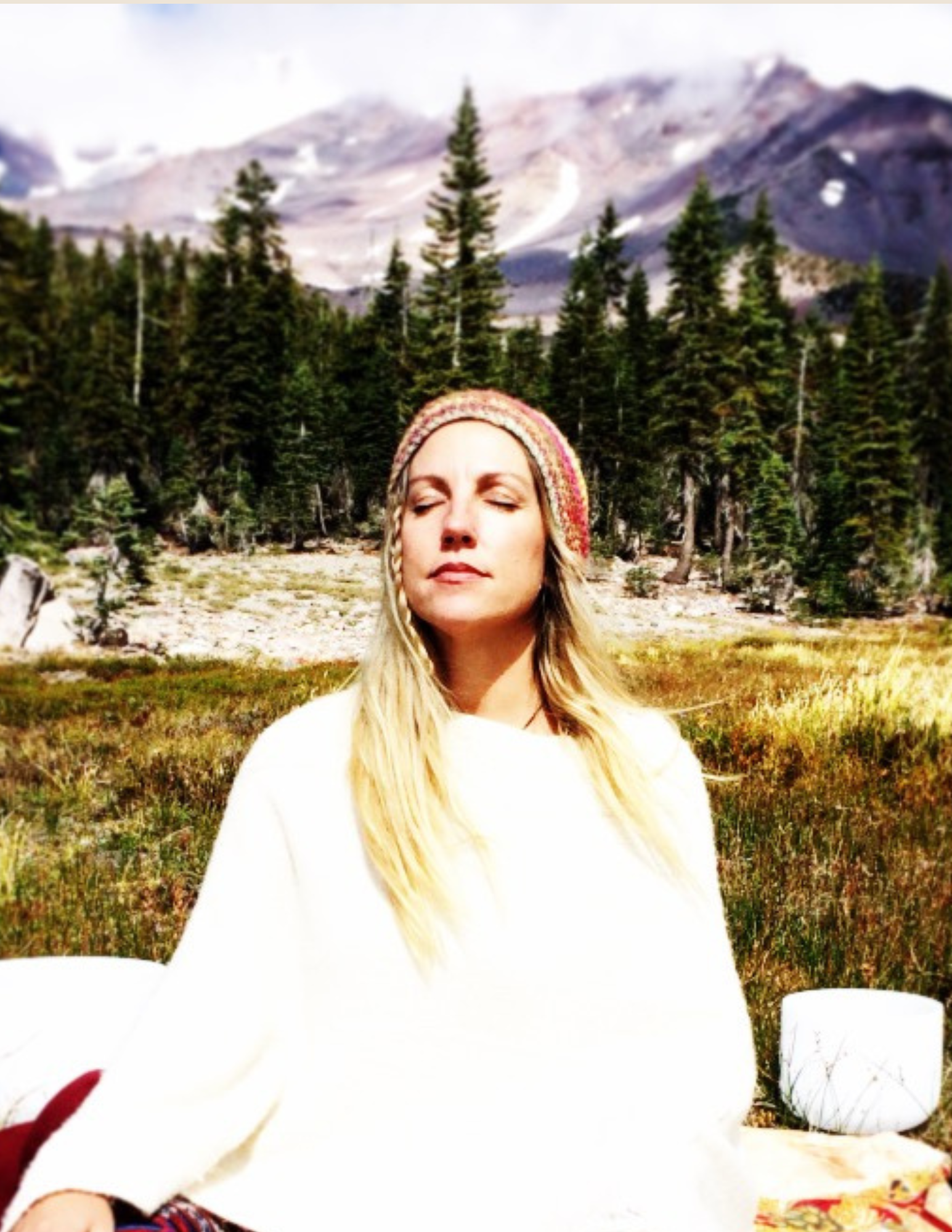 Woman meditating outdoors in nature with mountains and trees in the background.