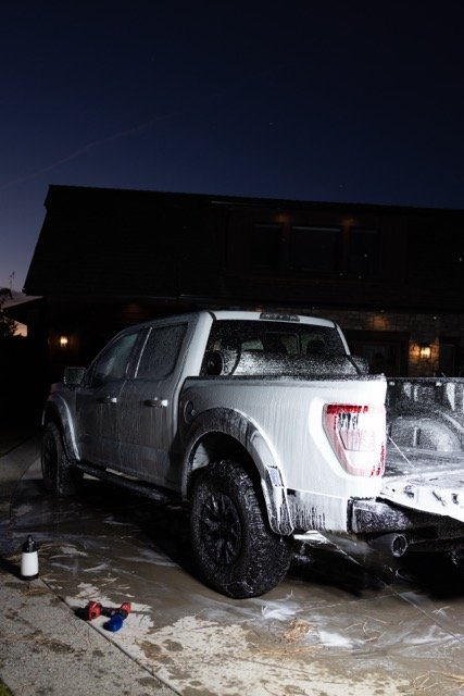 White pickup truck covered in soap suds, parked on a driveway at night.