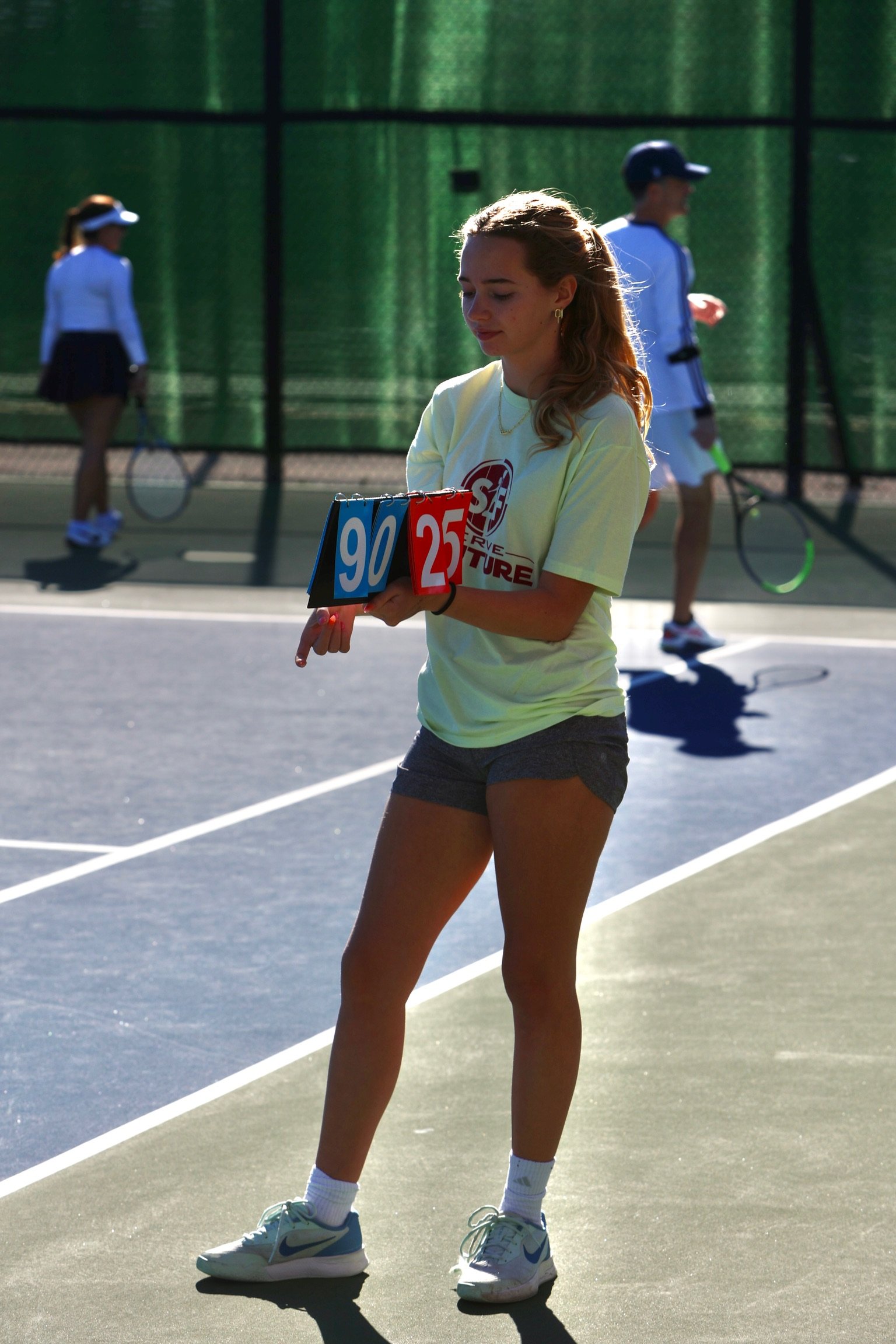 Female tennis line judge holding a scorecard with 90 and 25 on a tennis court during a match.