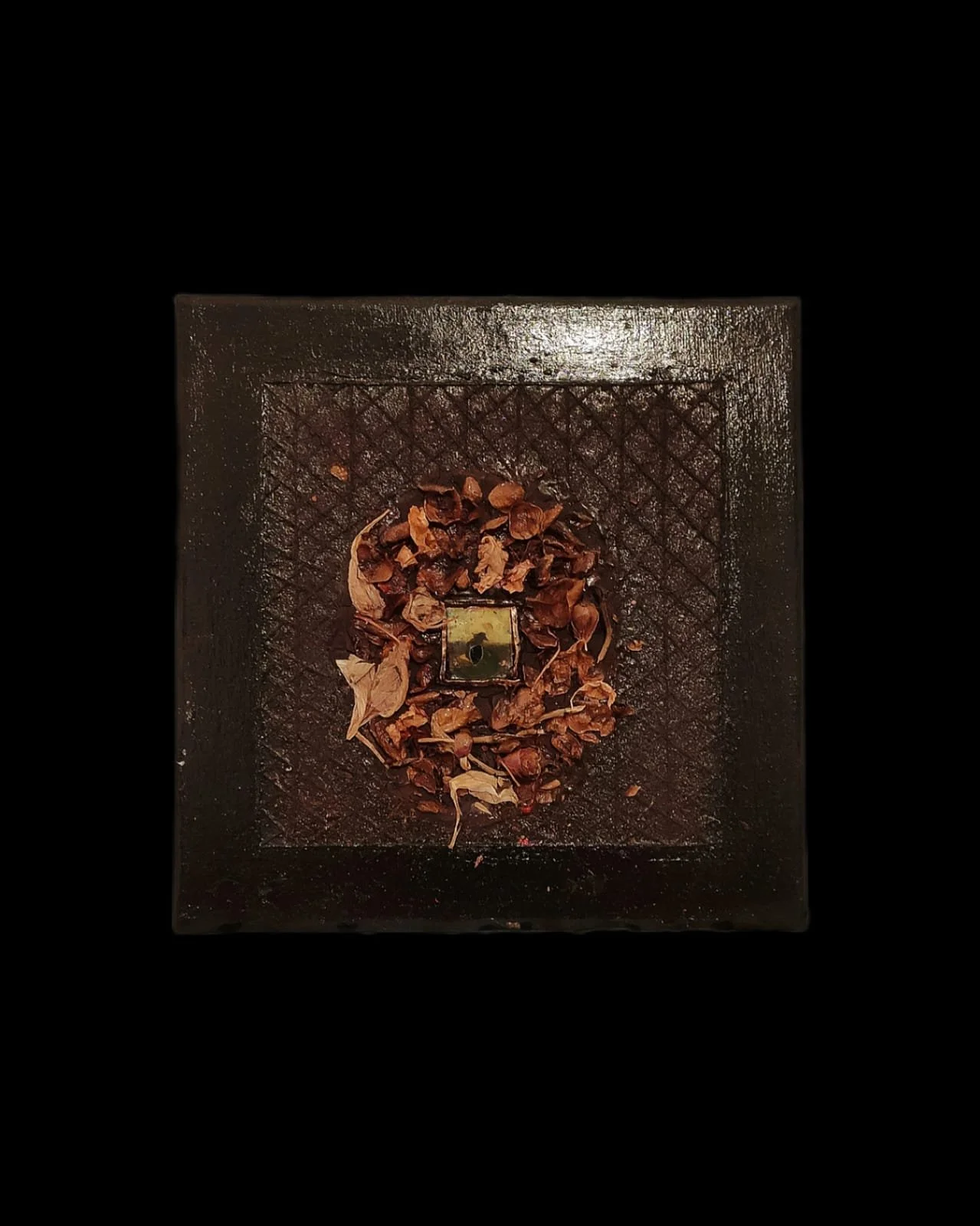 Decorative square tray with dried leaves and flowers arranged around a central small green object on lattice pattern background.