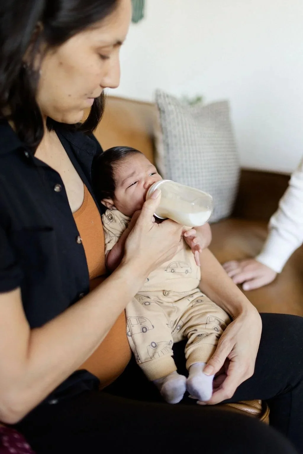 A woman is feeding a baby with a bottle of milk while sitting on a couch.