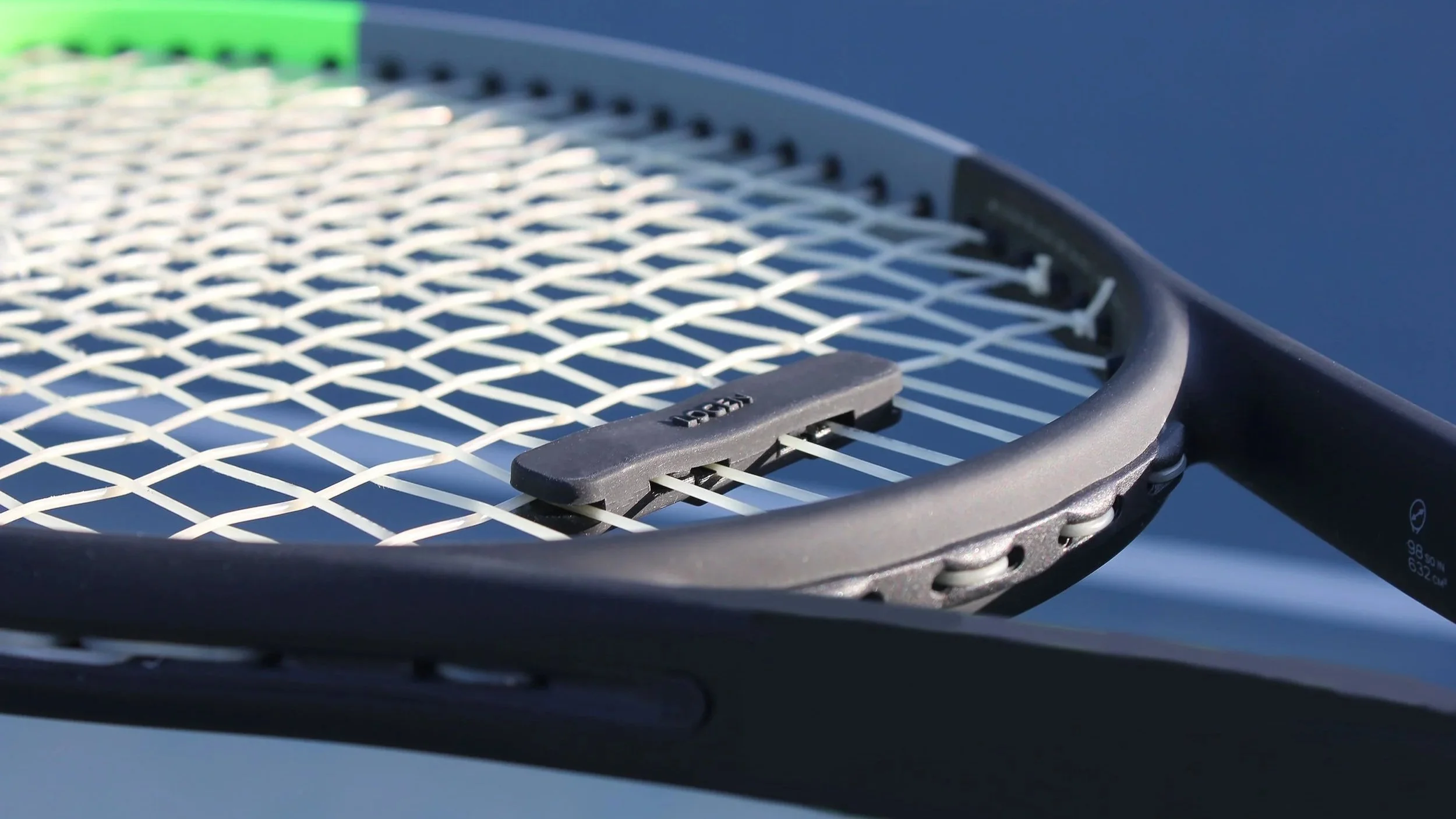 Close-up of a tennis racket with a black frame and white strings, resting on a gray surface.