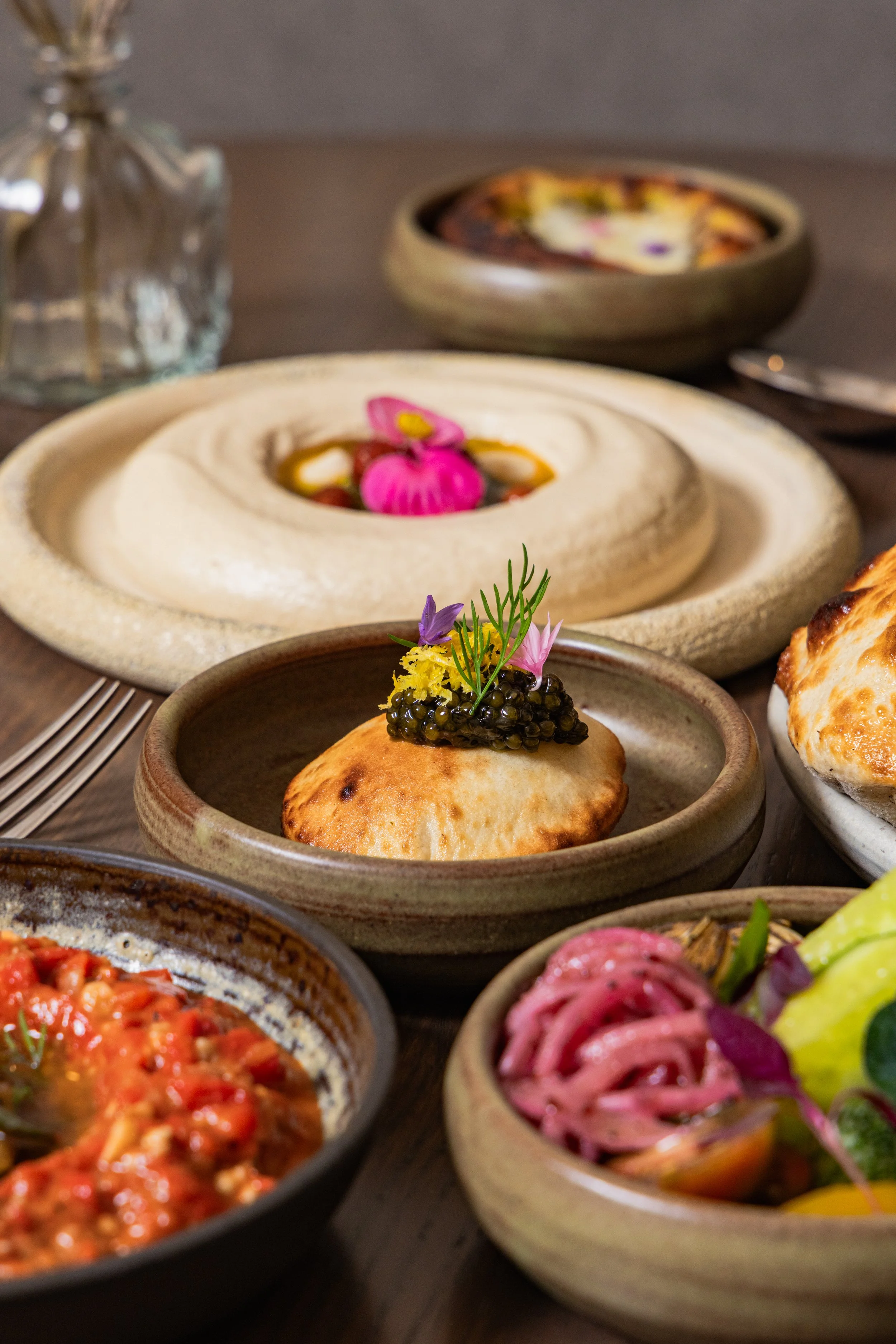 Assorted dishes with colorful garnishes, including a baked pastry topped with caviar and flowers, served in rustic bowls on a wooden table.