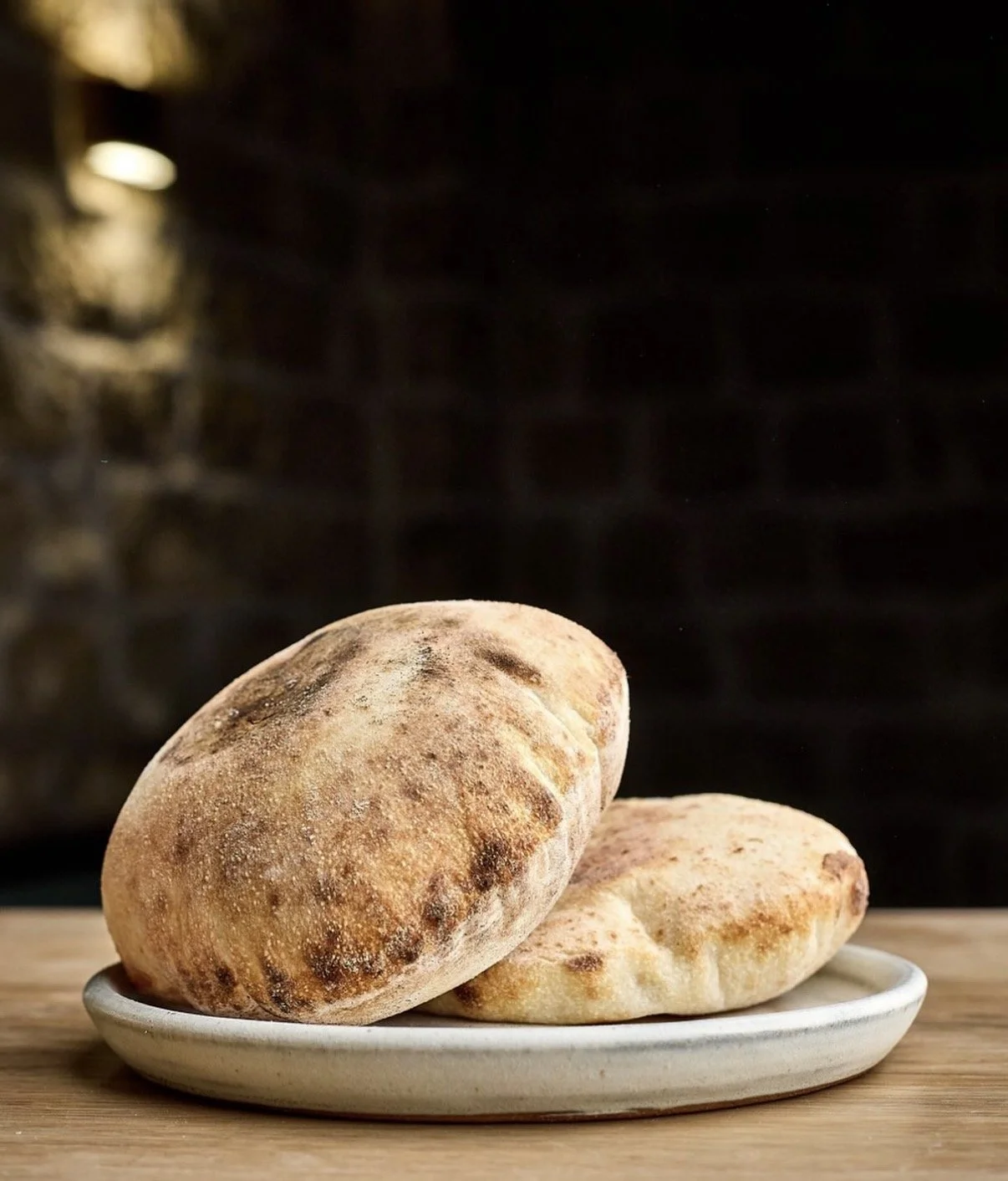 Two rustic bread rolls on a white plate, placed on a wooden surface, with a dark, blurred background.