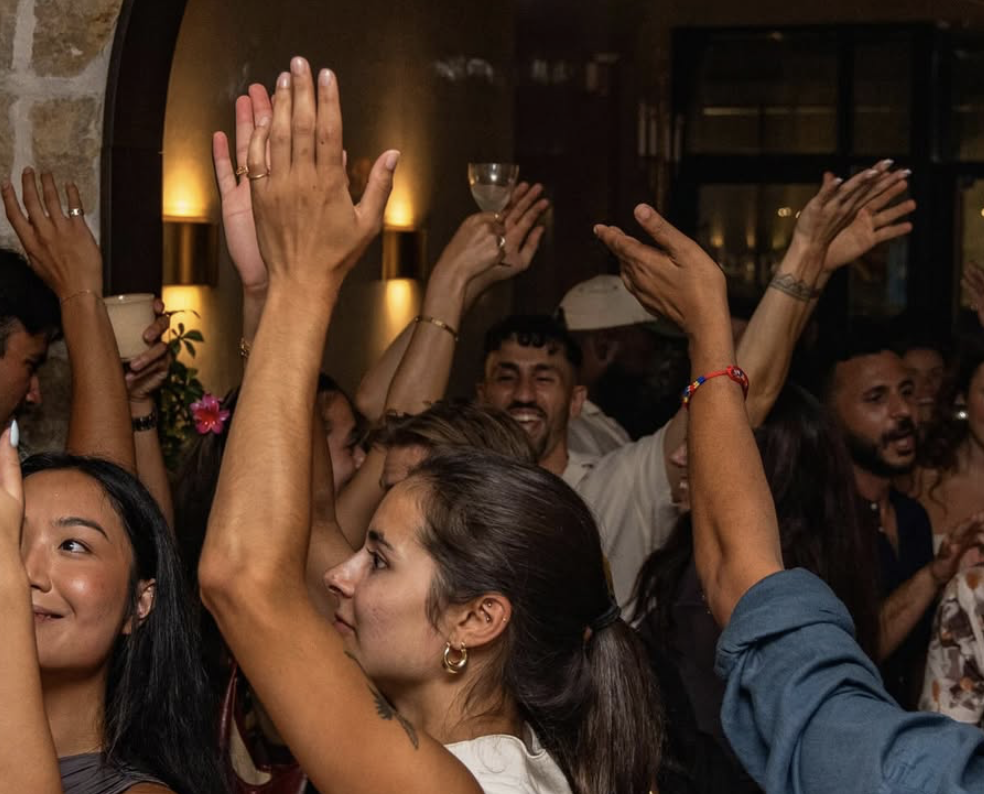 People dancing and celebrating at a party, raising their hands, with a lively atmosphere and warm lighting.