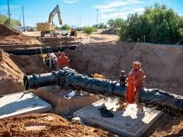 Construction site with large piping and a worker in safety gear installing equipment