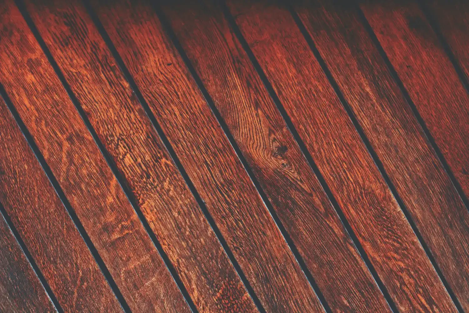 Close-up view of wooden floorboards stained in dark reddish-brown with a glossy finish.
